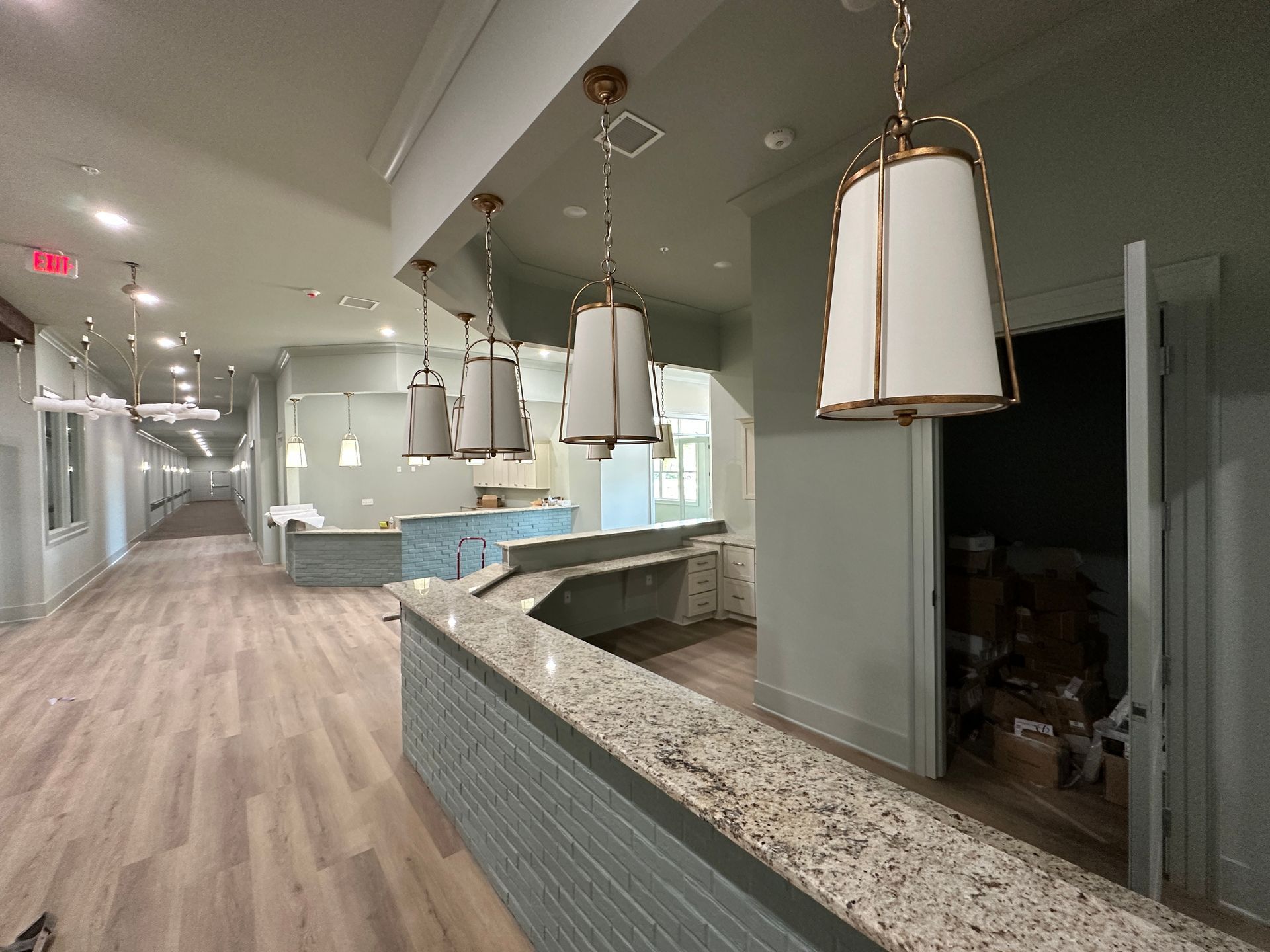 Modern hallway featuring light wood floors, a long service counter with a granite top, and hanging pendant lights.