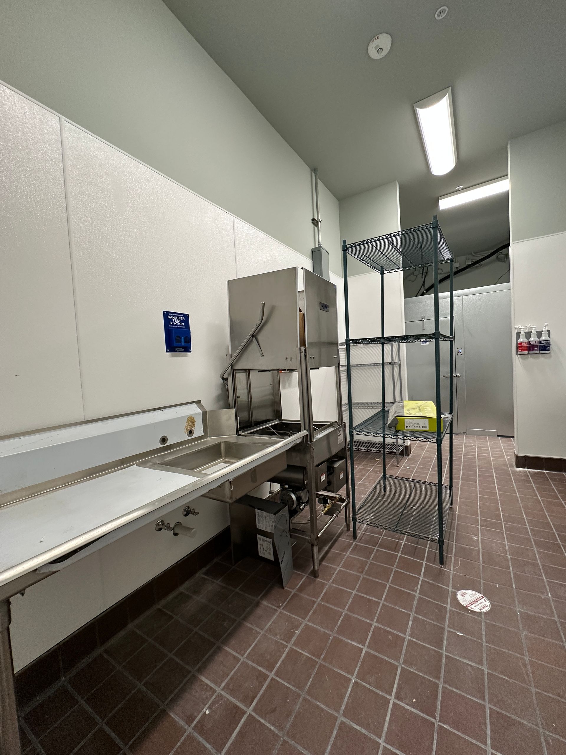A commercial dishwashing area featuring a stainless steel sink, a hood system, and a wire shelving unit on a tiled floor.