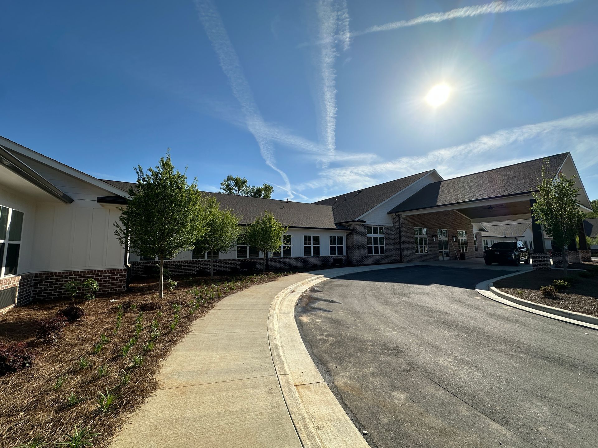 A modern, one-story commercial building with light siding, dark roof, and a paved circular drive under a clear blue sky.