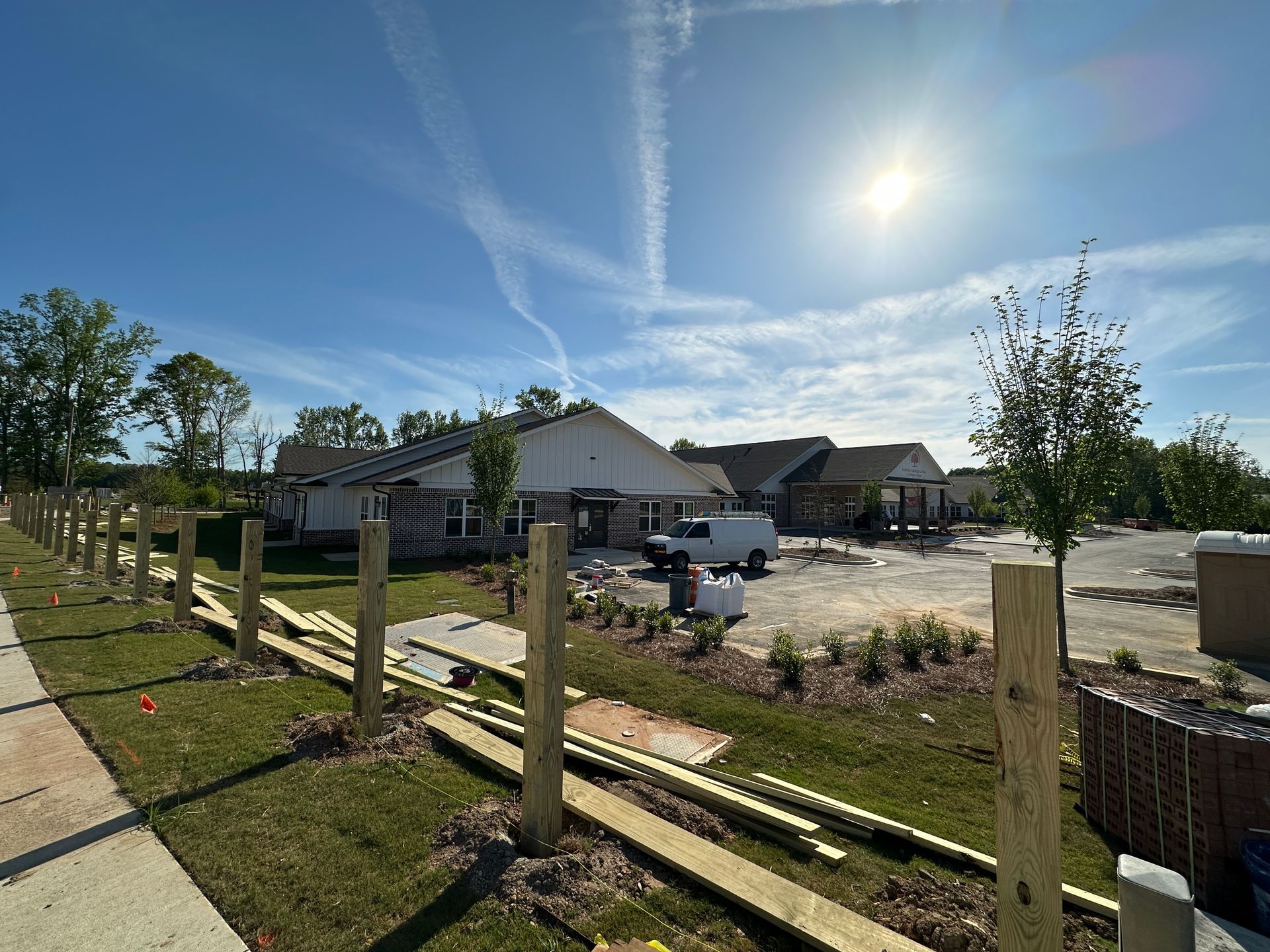 Newly built houses under a bright sun, featuring a wooden fence under construction in the foreground.