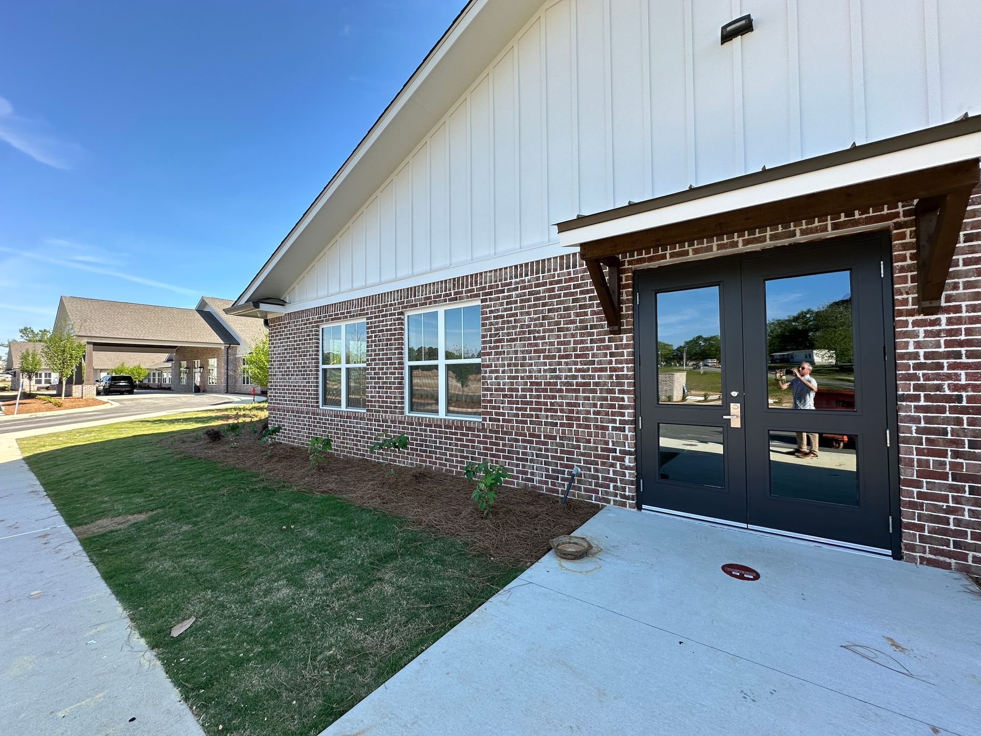 A brick building with a double-door entrance, concrete walkway, and landscaped lawn under a clear blue sky.