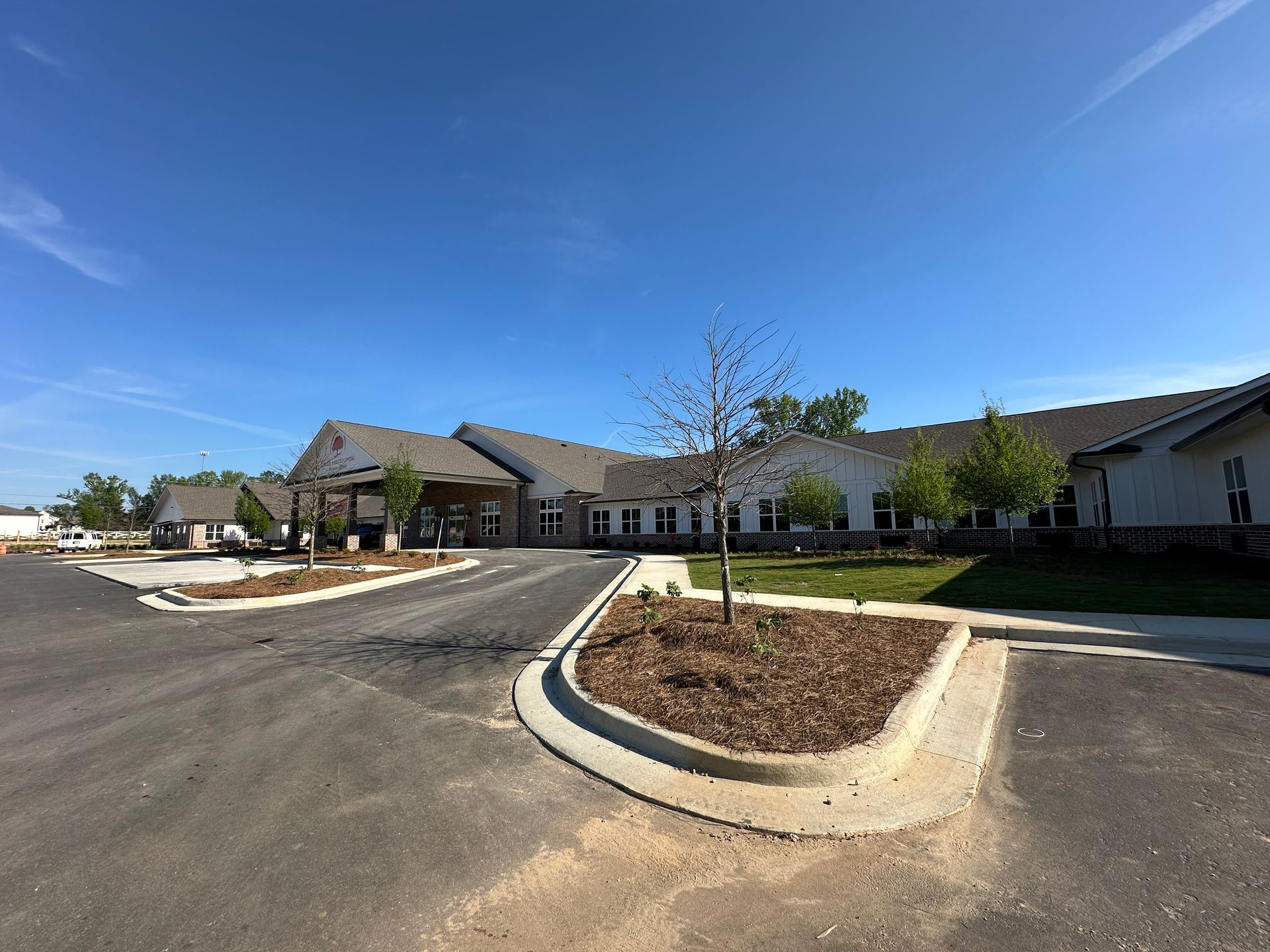 A newly constructed one-story building with a light gray facade, covered entryway, and a landscaped circular driveway.