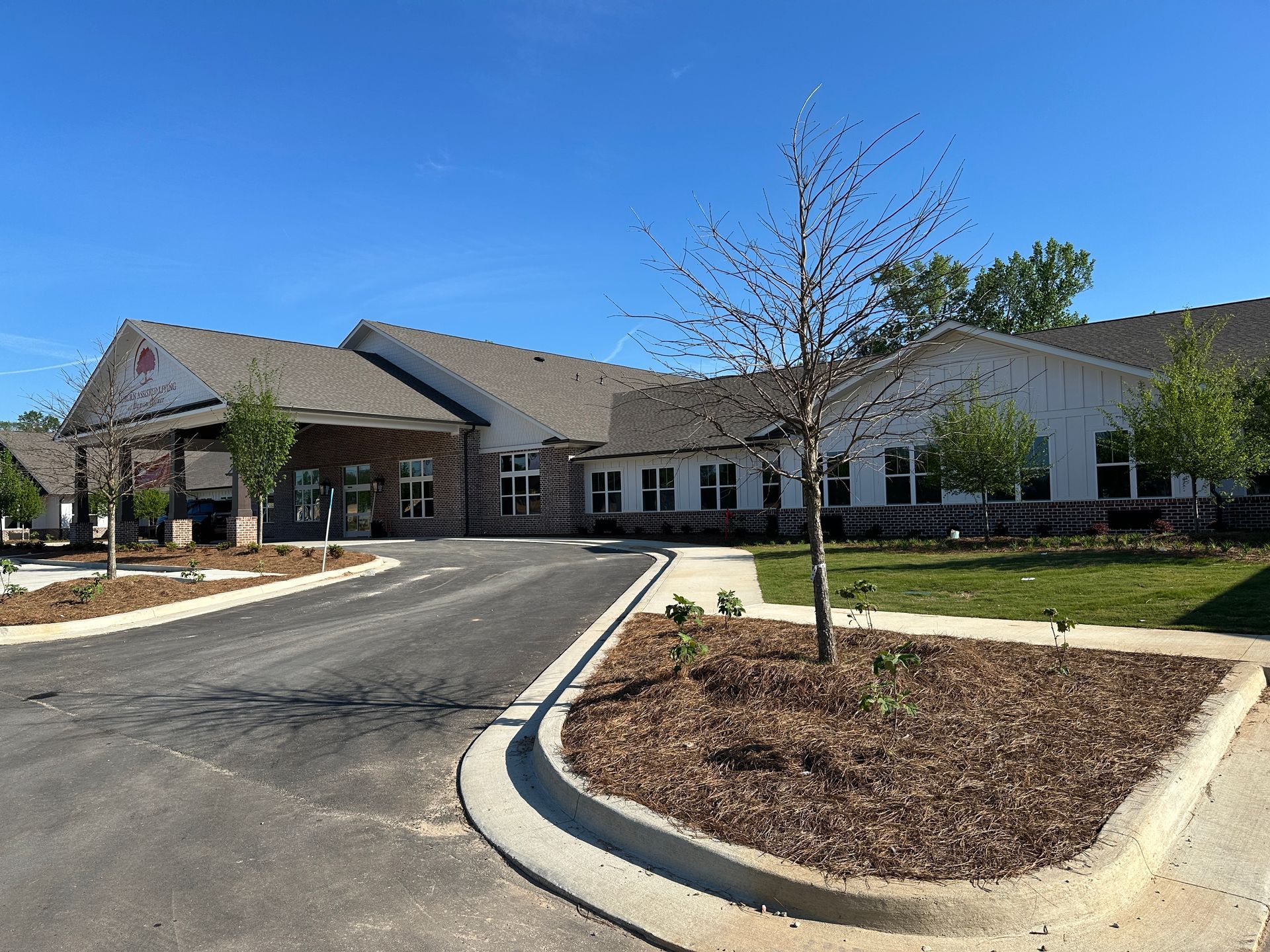 A newly constructed single-story building with a covered entrance, a paved driveway, and mulched landscaping under blue sky.