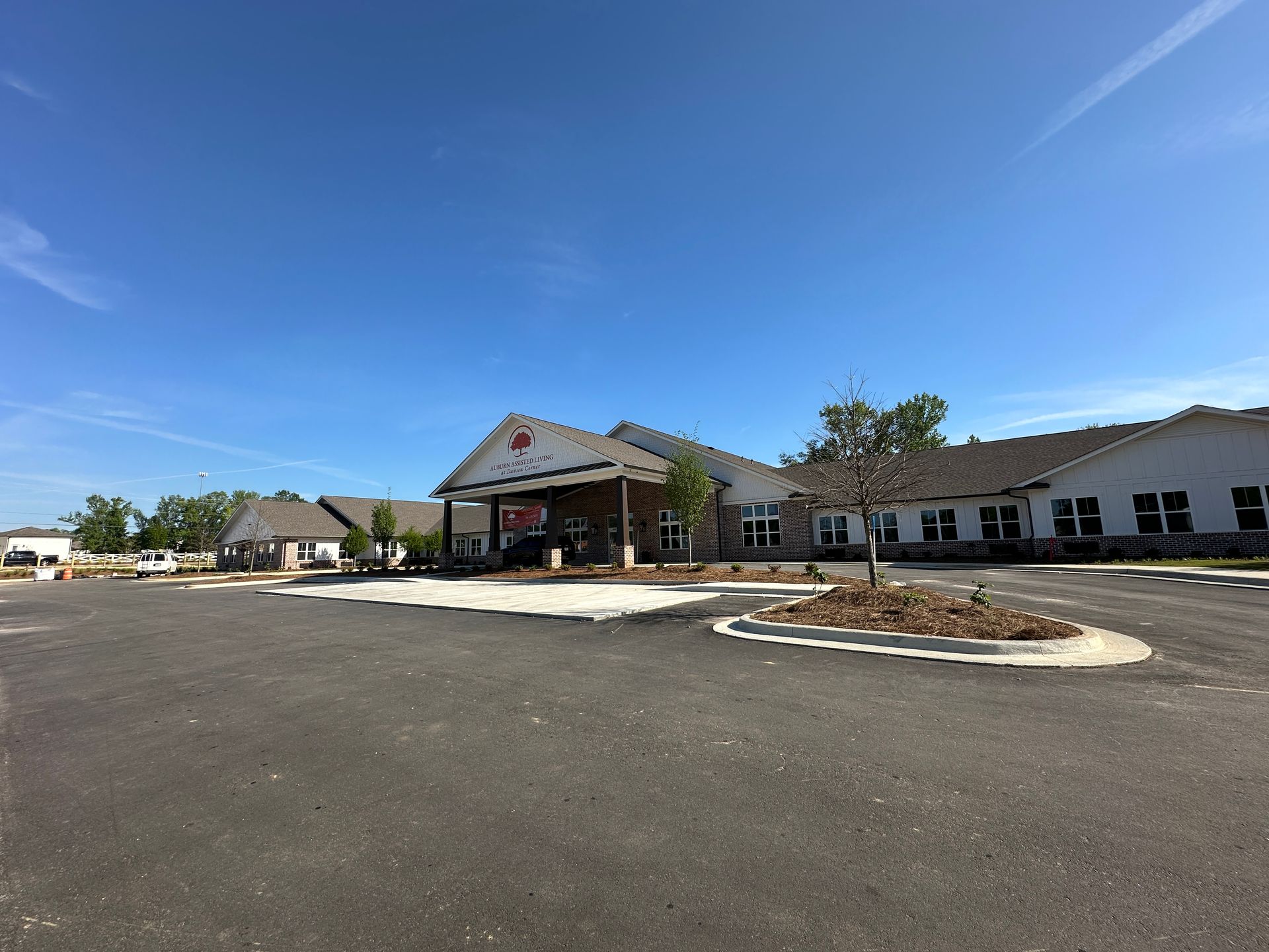 A long, one-story commercial building with white siding and stone accents under a clear blue sky, seen from a parking lot.