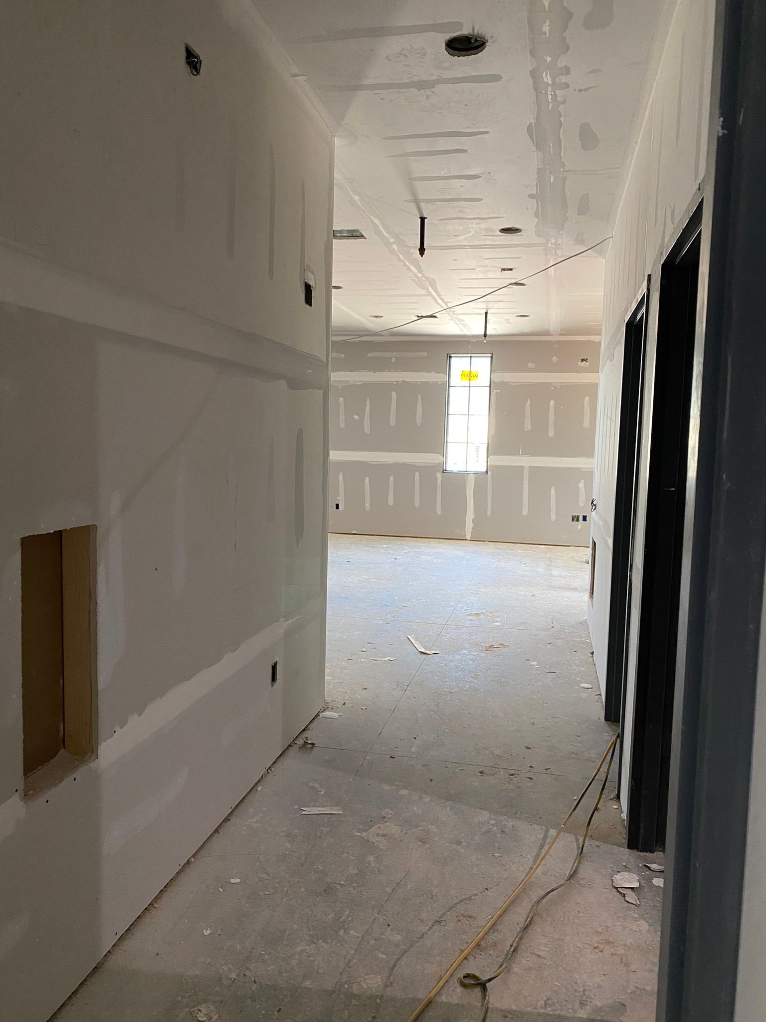 A long hallway with drywall walls and a window
