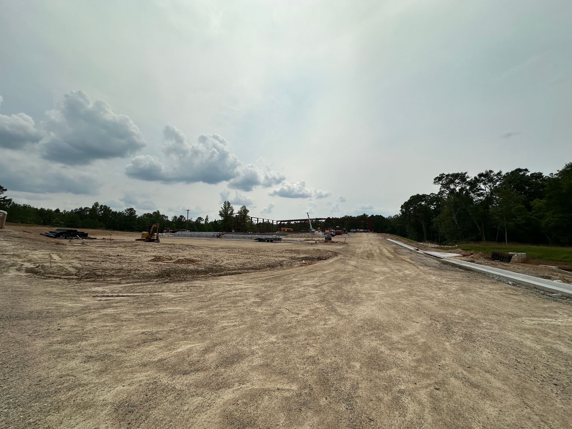 A dirt road with trees on the side and a cloudy sky in the background.
