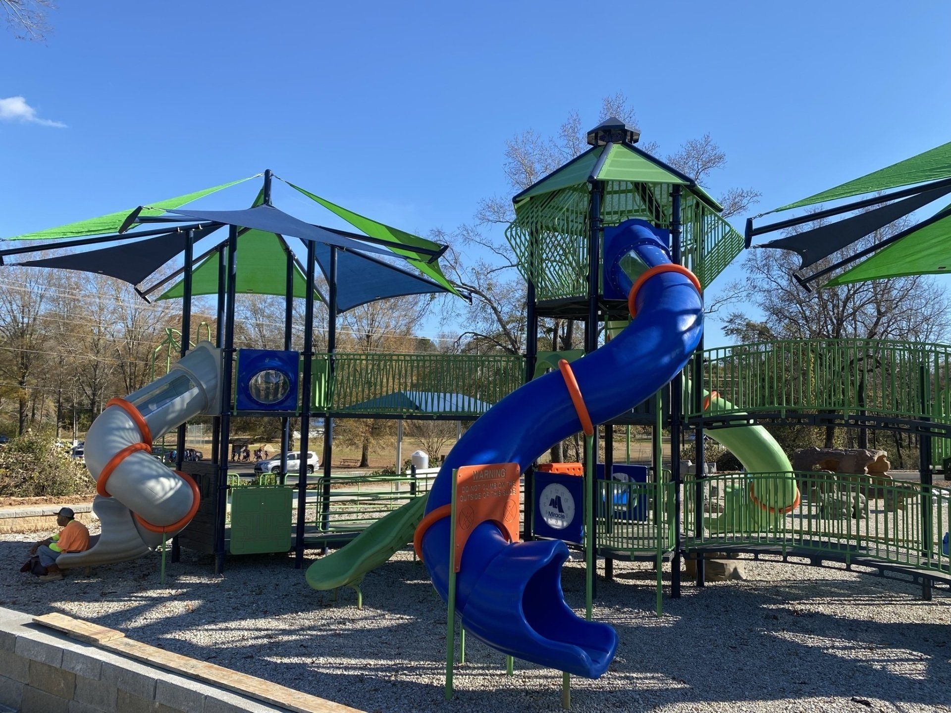 A playground with a blue slide and green umbrellas.