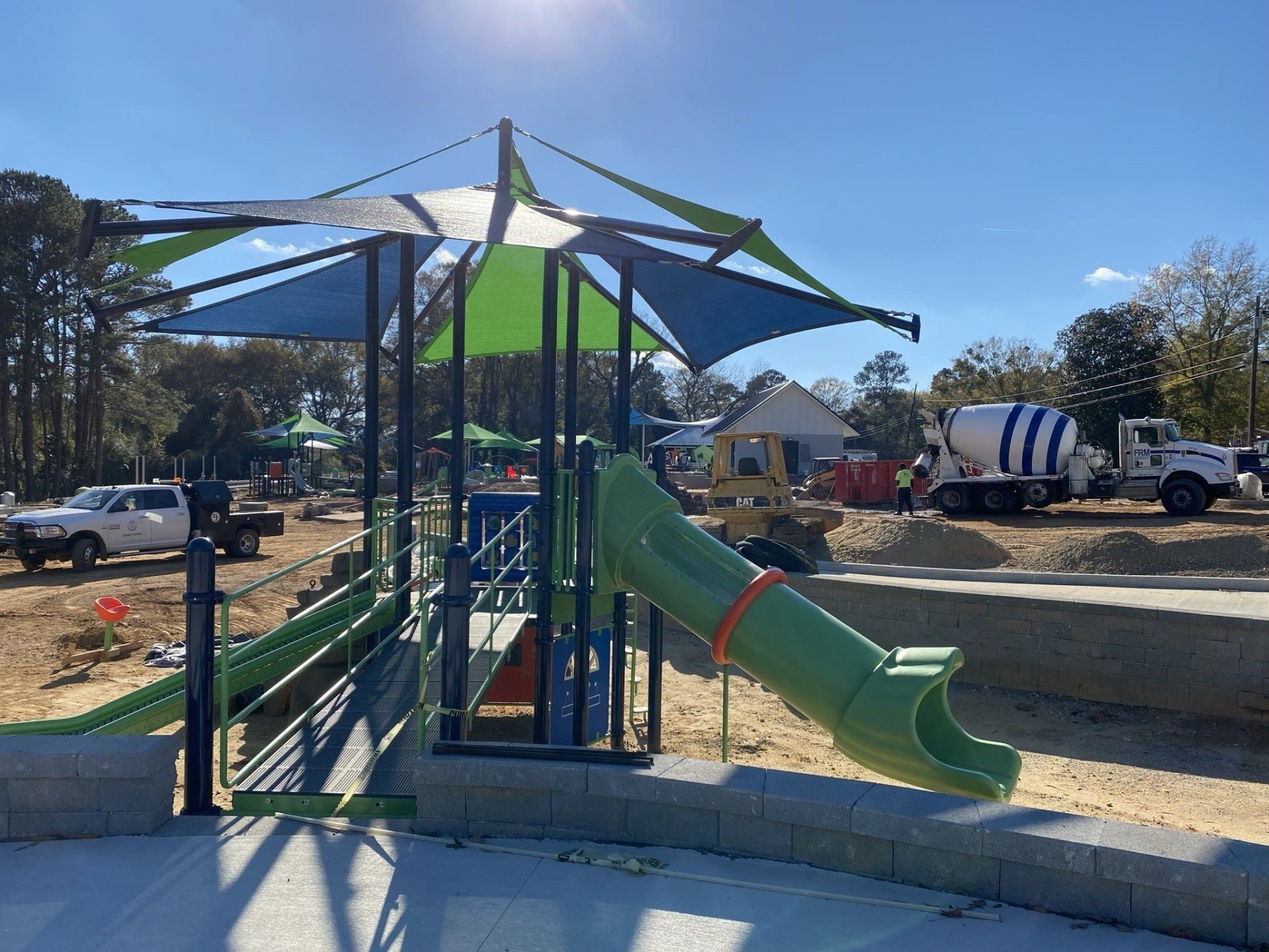 A green slide is sitting under an umbrella in a park.