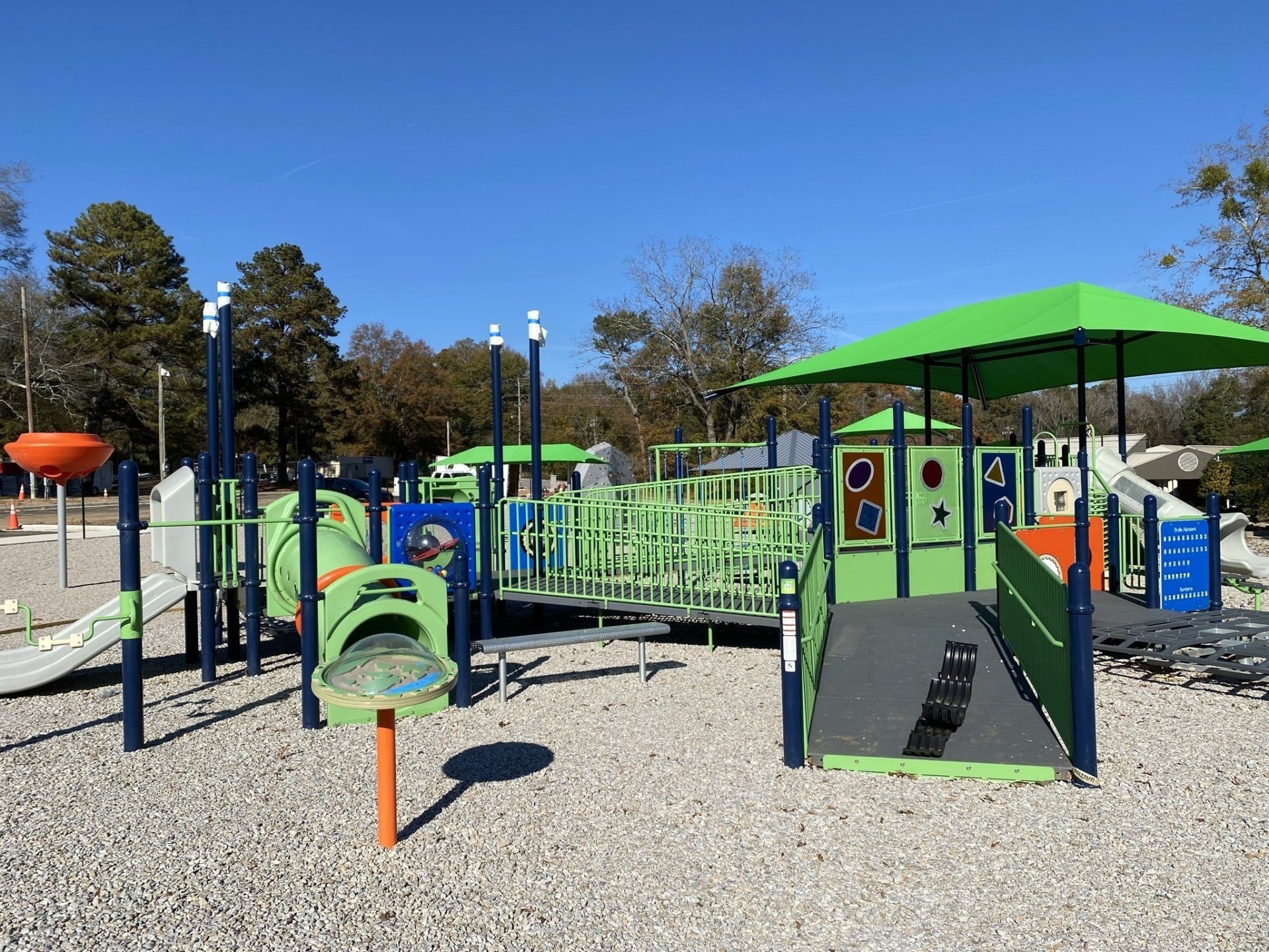 A playground with a green umbrella and a ramp.