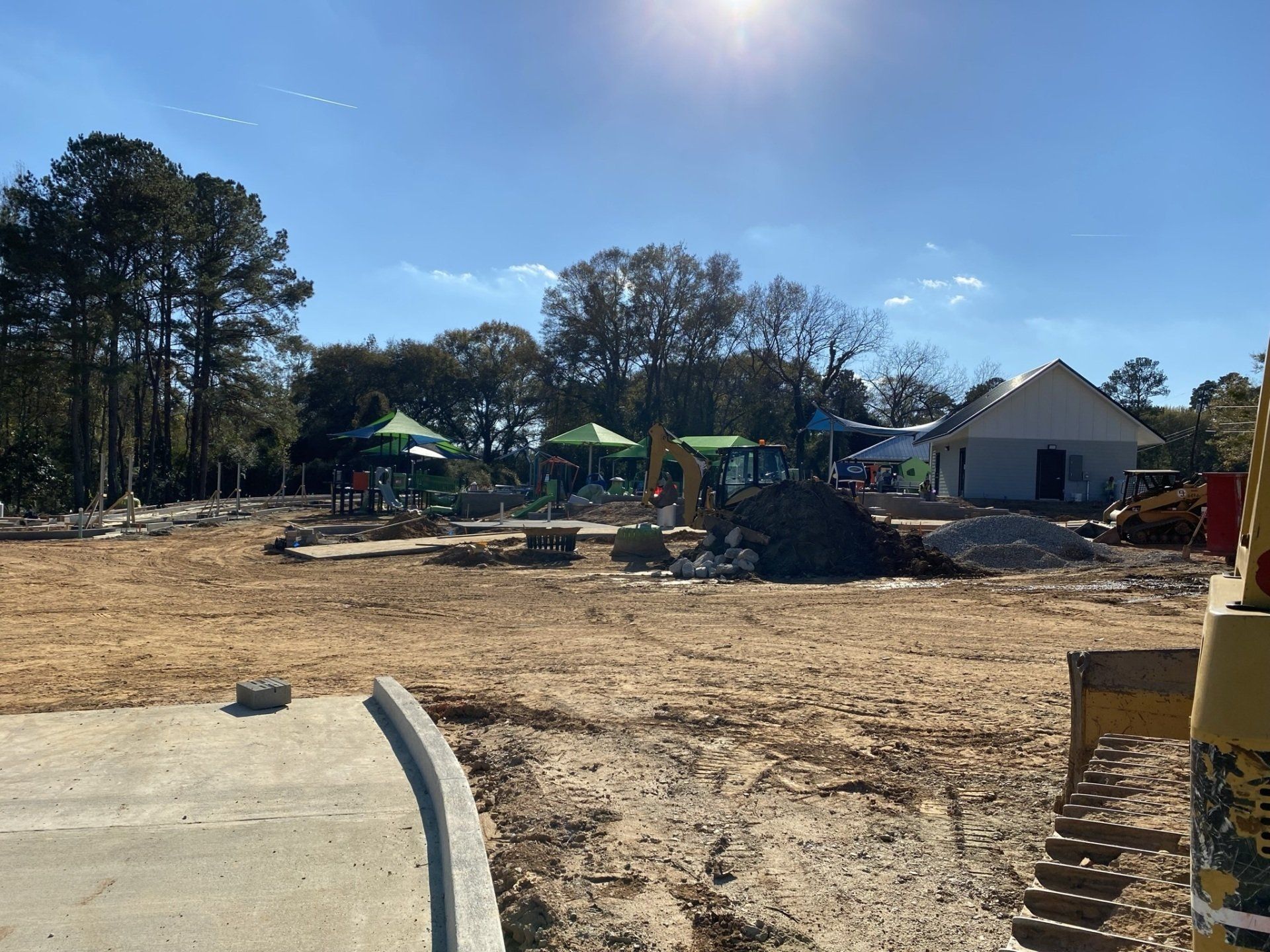 A construction site with a playground in the background and a bulldozer in the foreground.