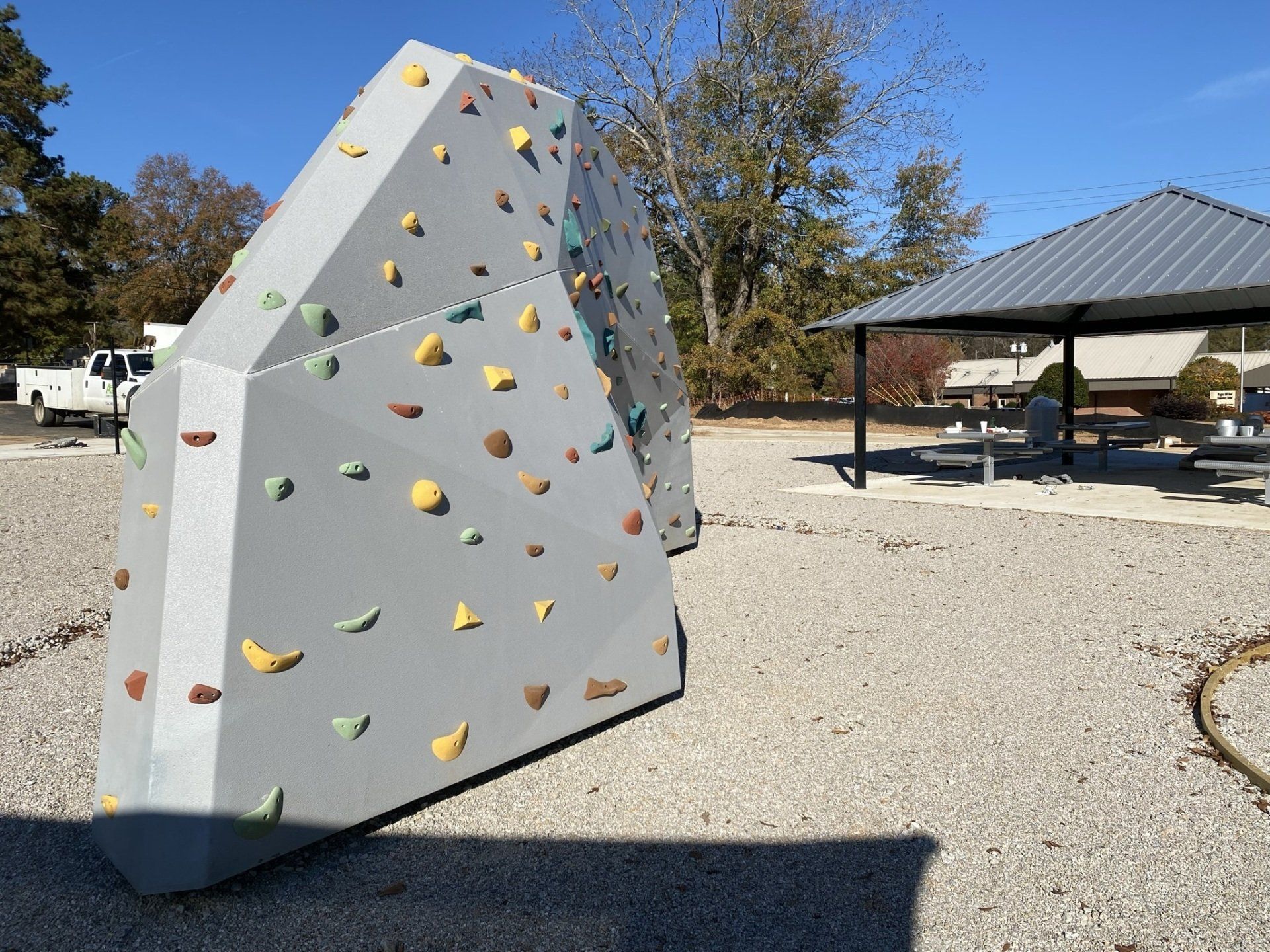 A climbing wall in a gravel area with a pavilion in the background