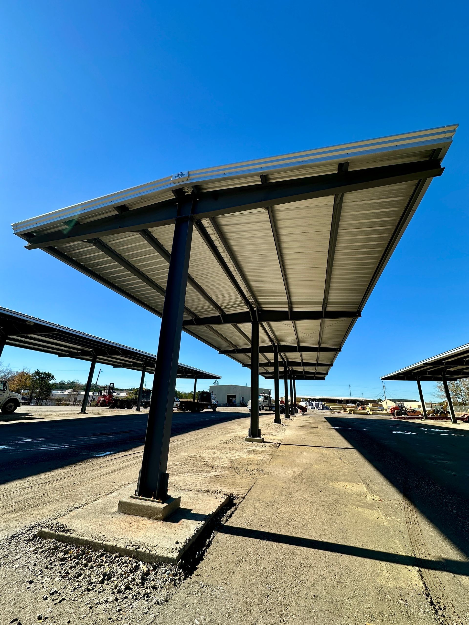Solar panel carport structure with gray metal roof on concrete pillars, blue sky.