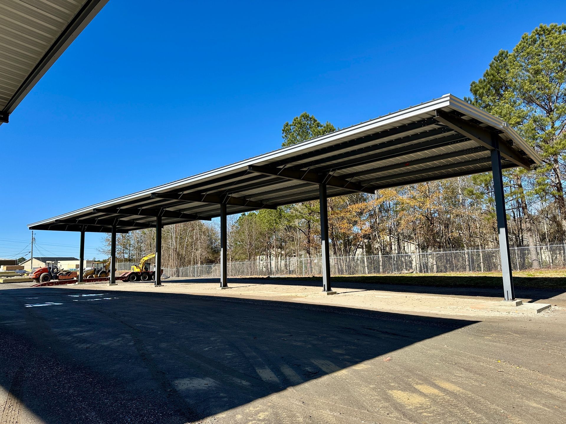 Long, metal carport with a corrugated roof, under a clear, blue sky.