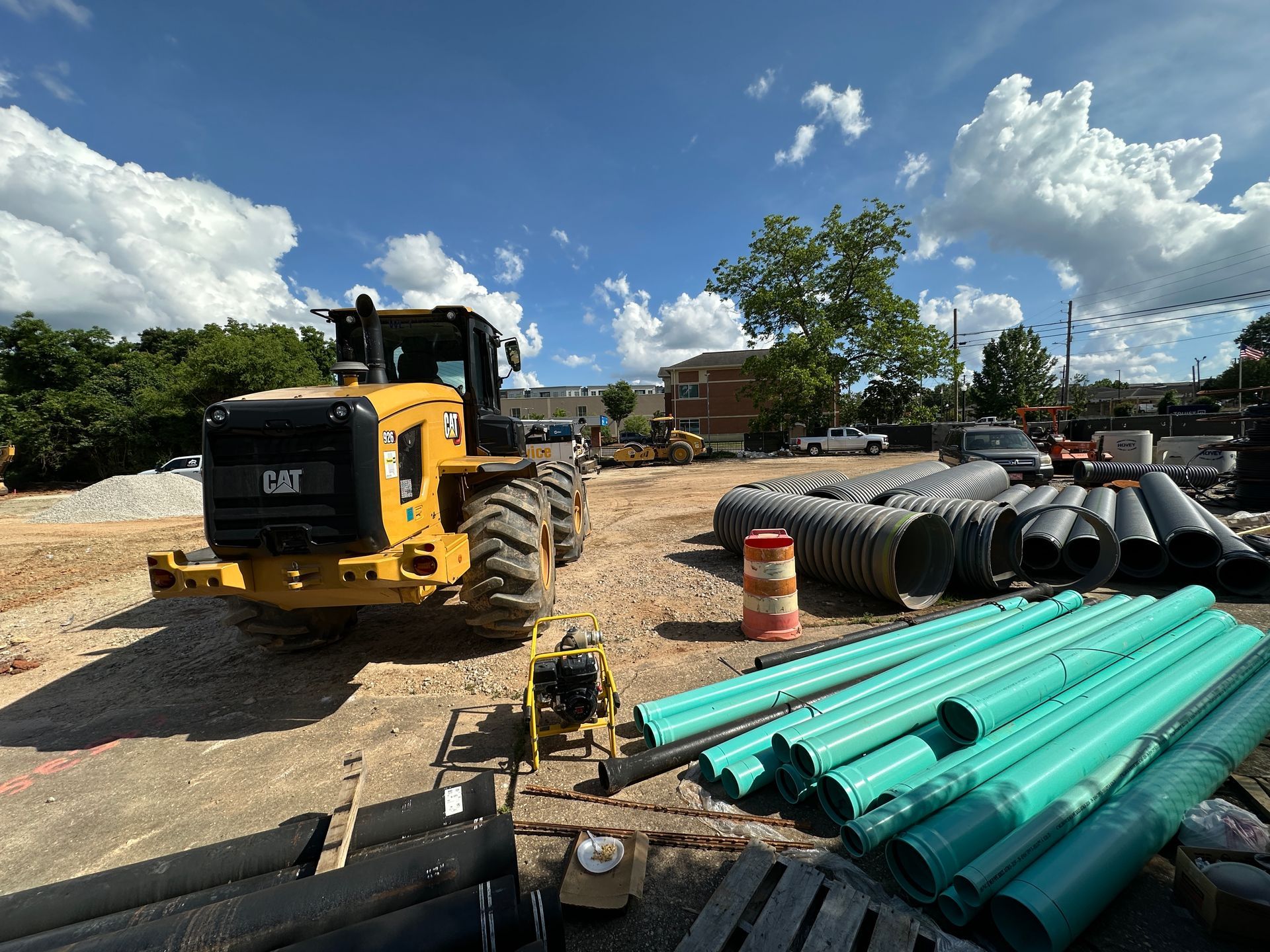 Construction site with yellow loader and stacked green pipes under a cloudy sky