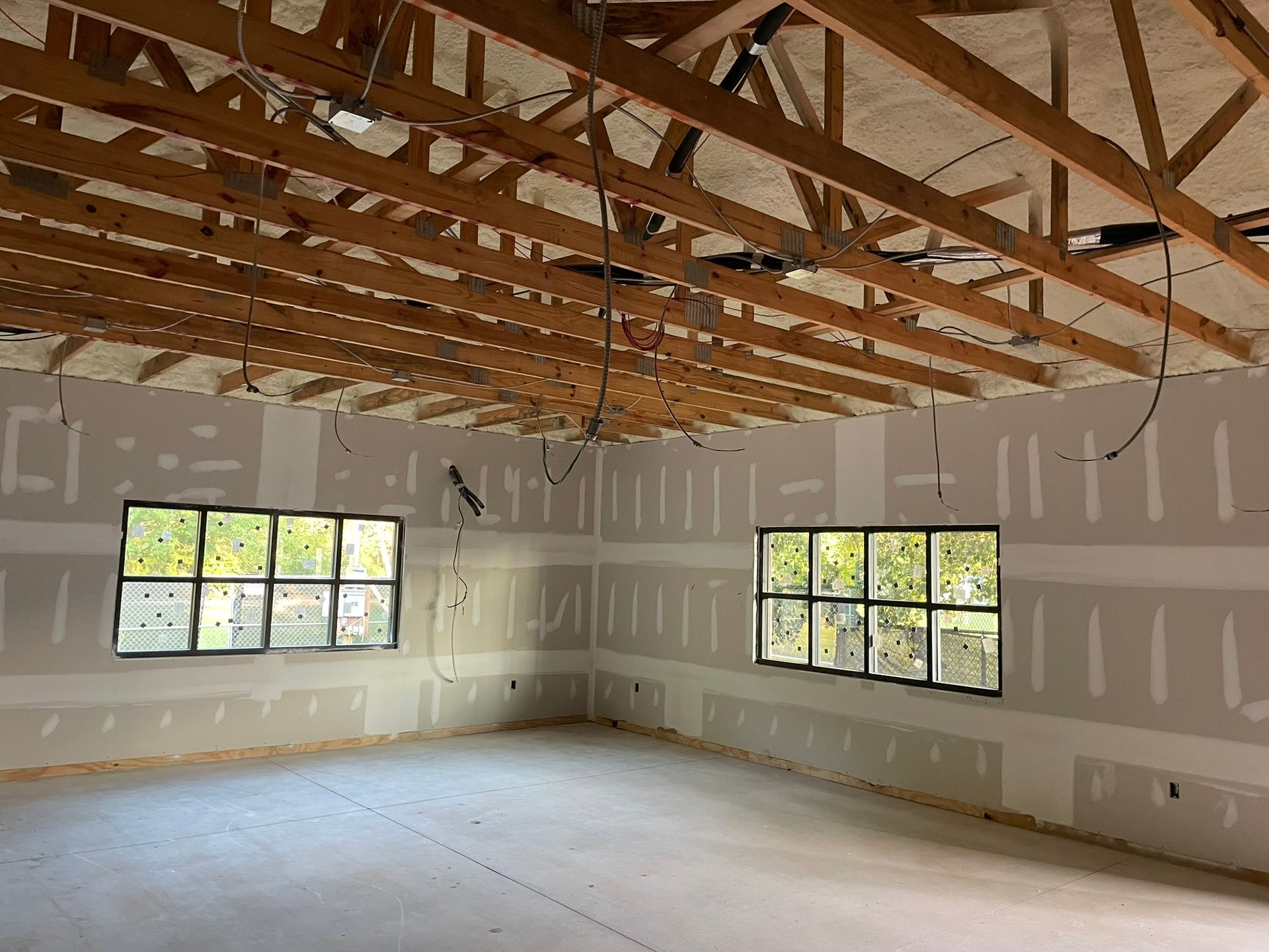 Interior of a room under construction with exposed rafters, drywall, windows, and wiring.