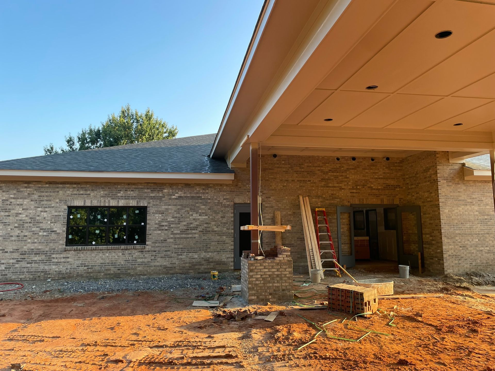 Exterior of a brick building under construction; red dirt, a ladder, and a large window are visible.