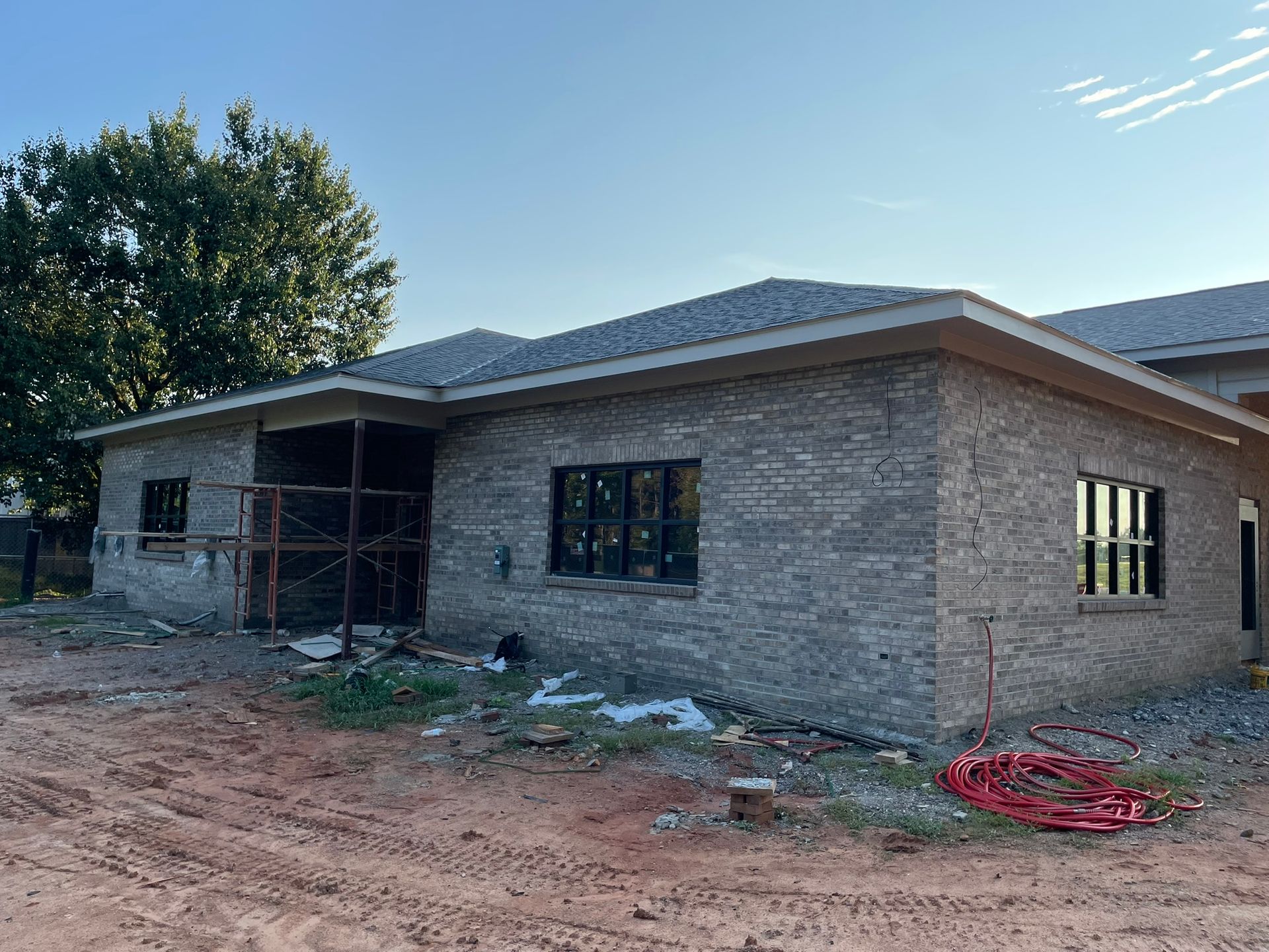 Exterior of a house under construction with brick siding, windows, and roof. Red tubing lies on the ground.