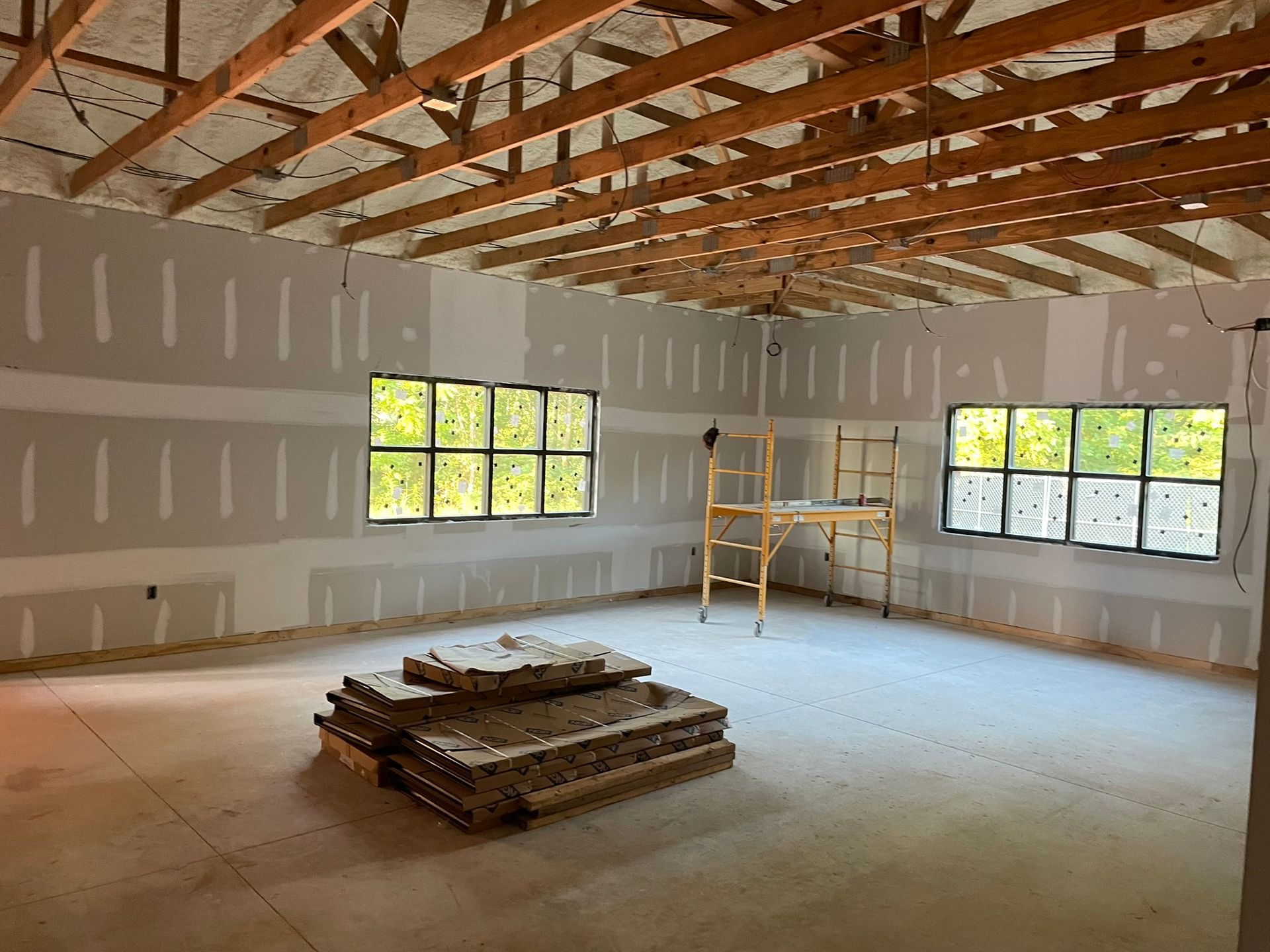 Interior of a room under construction with drywall, windows, and a wooden ceiling. Stack of insulation in foreground.