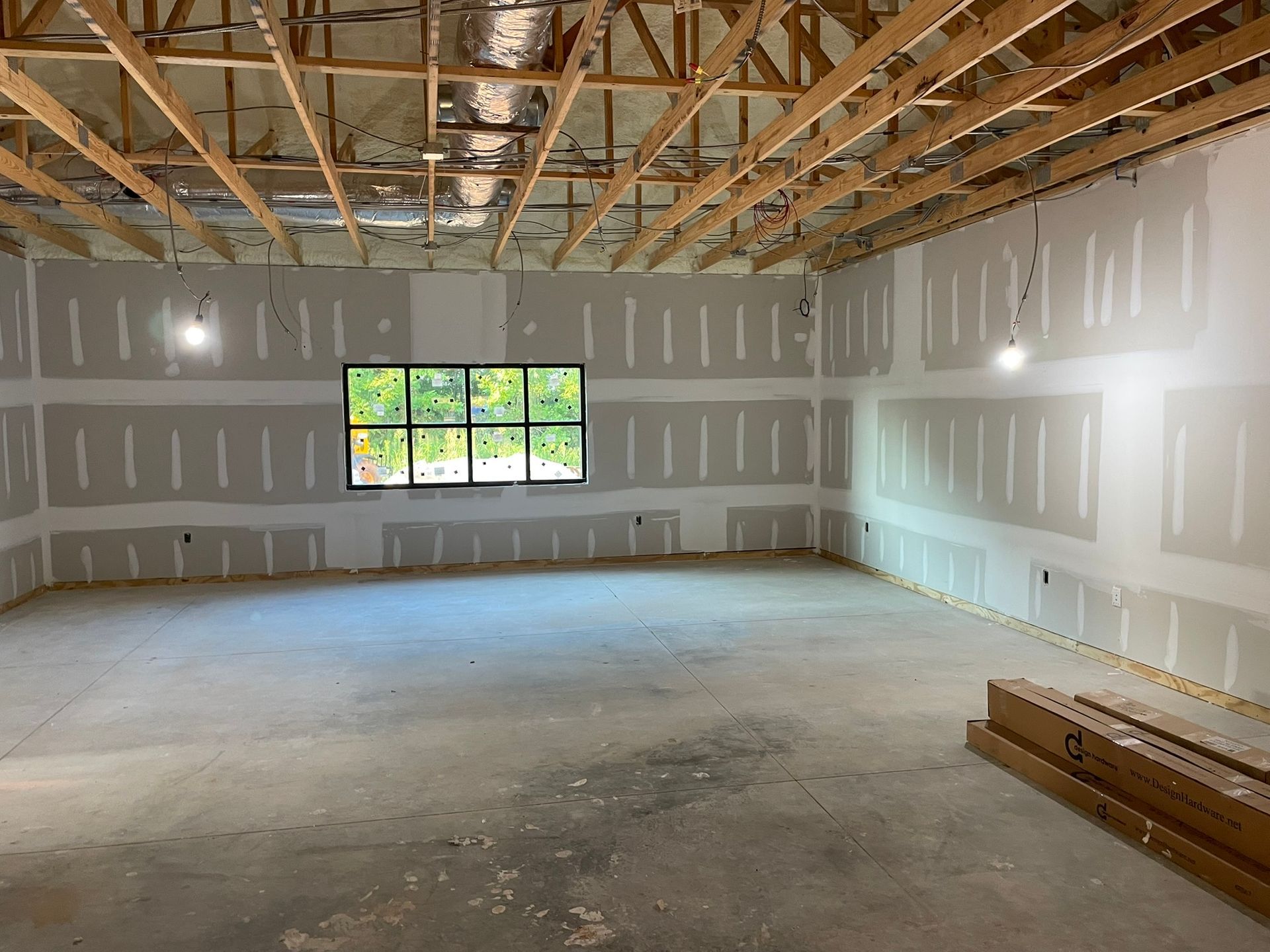 An unfinished interior with drywall, window, and exposed ceiling beams.