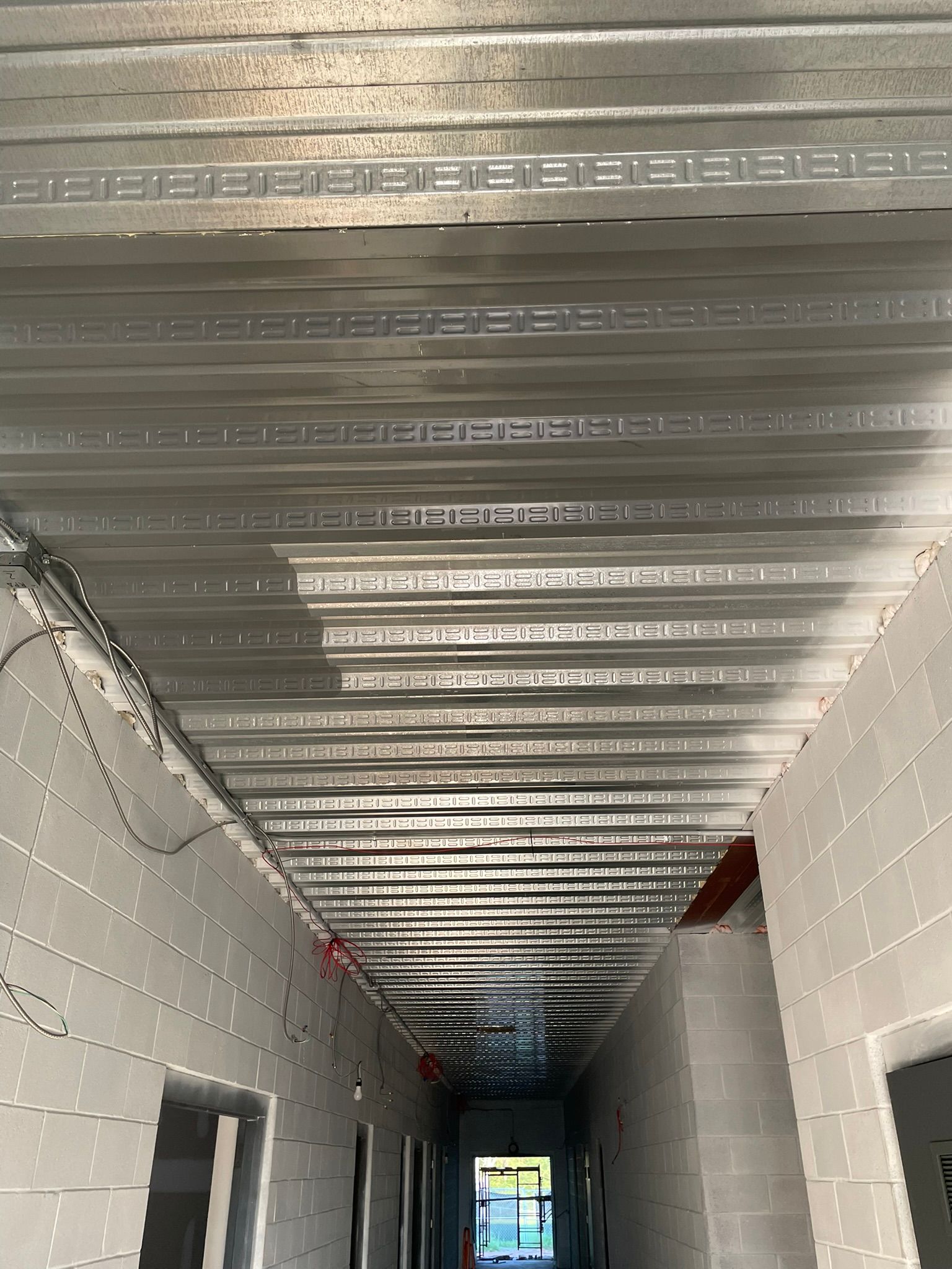 Metal ceiling beams in a narrow hallway under construction; cinder block walls.