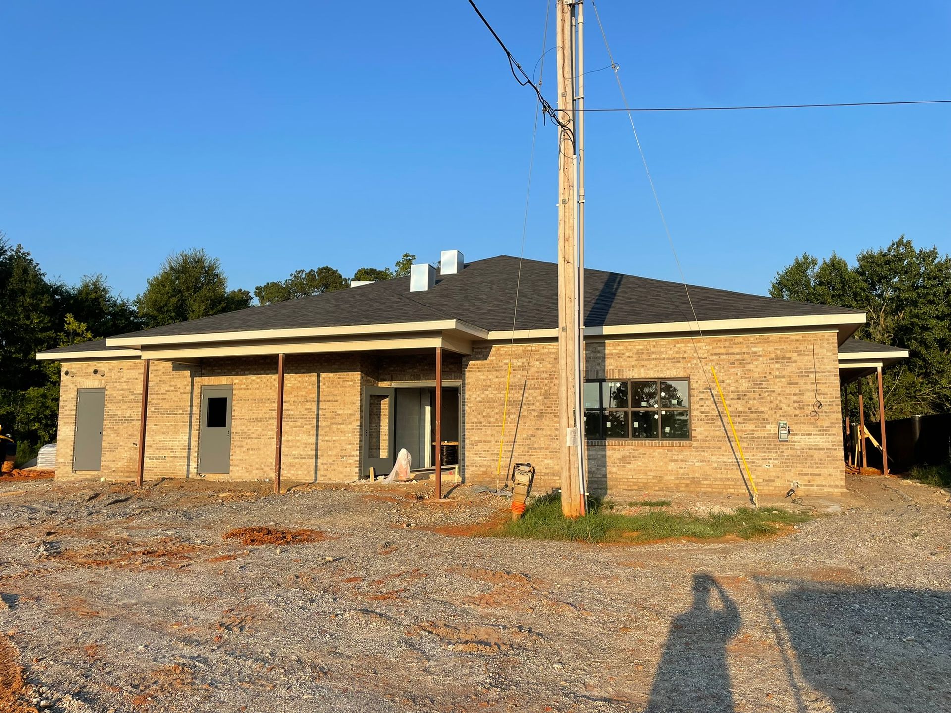 A one-story building under construction with brick-like walls, a dark roof, and an exposed wooden frame.