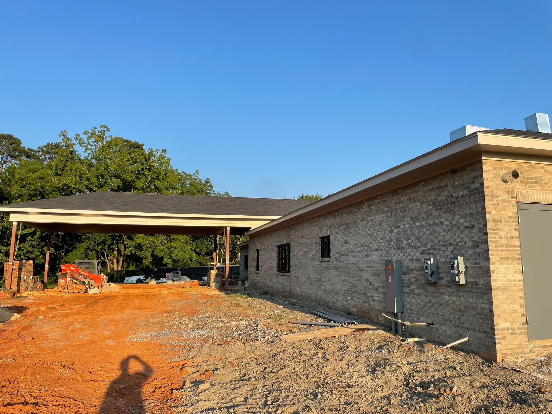 Construction site with a brick building and carport under a clear blue sky.
