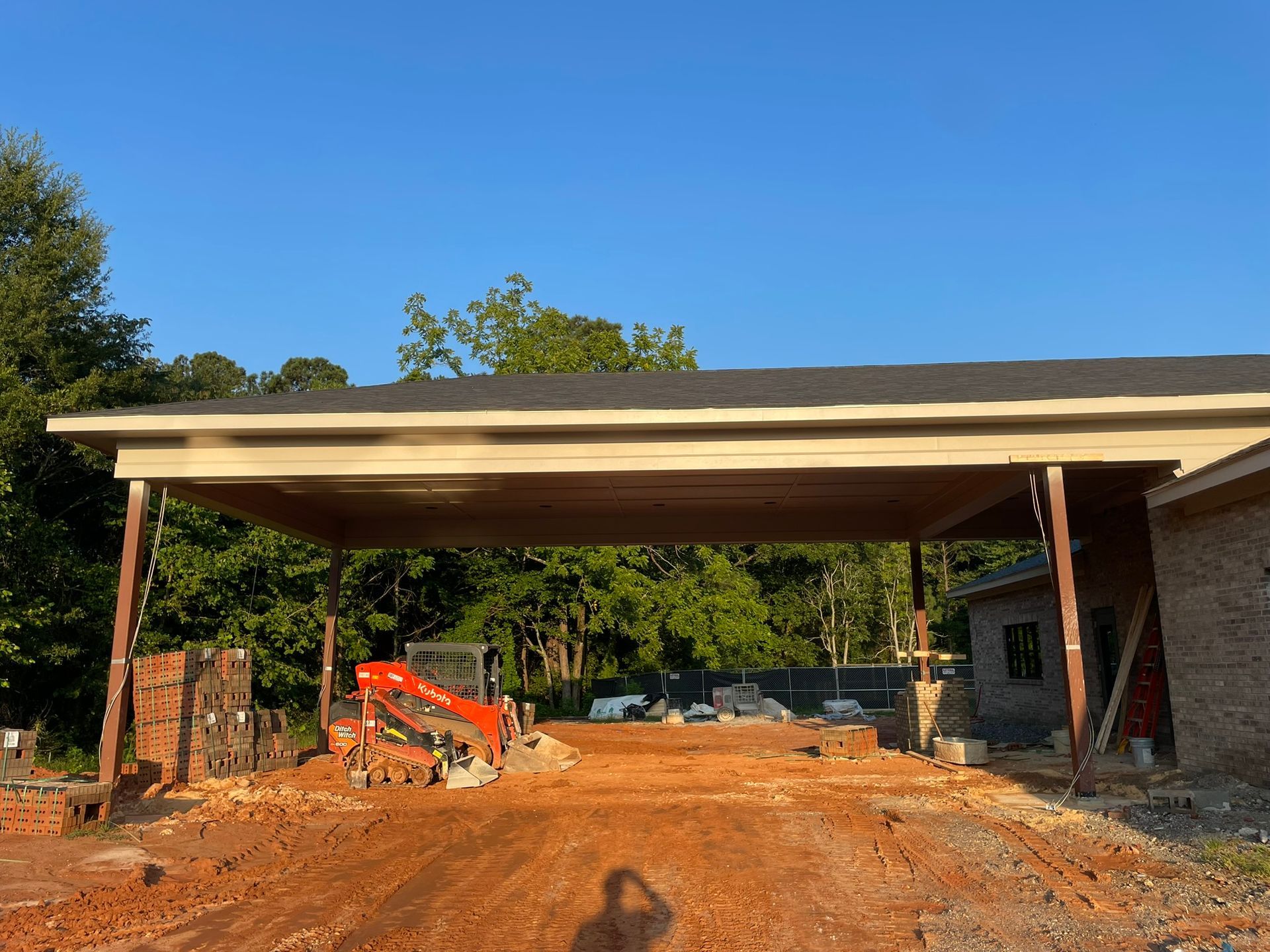 Construction site with a covered carport, dirt road, and clear blue sky.