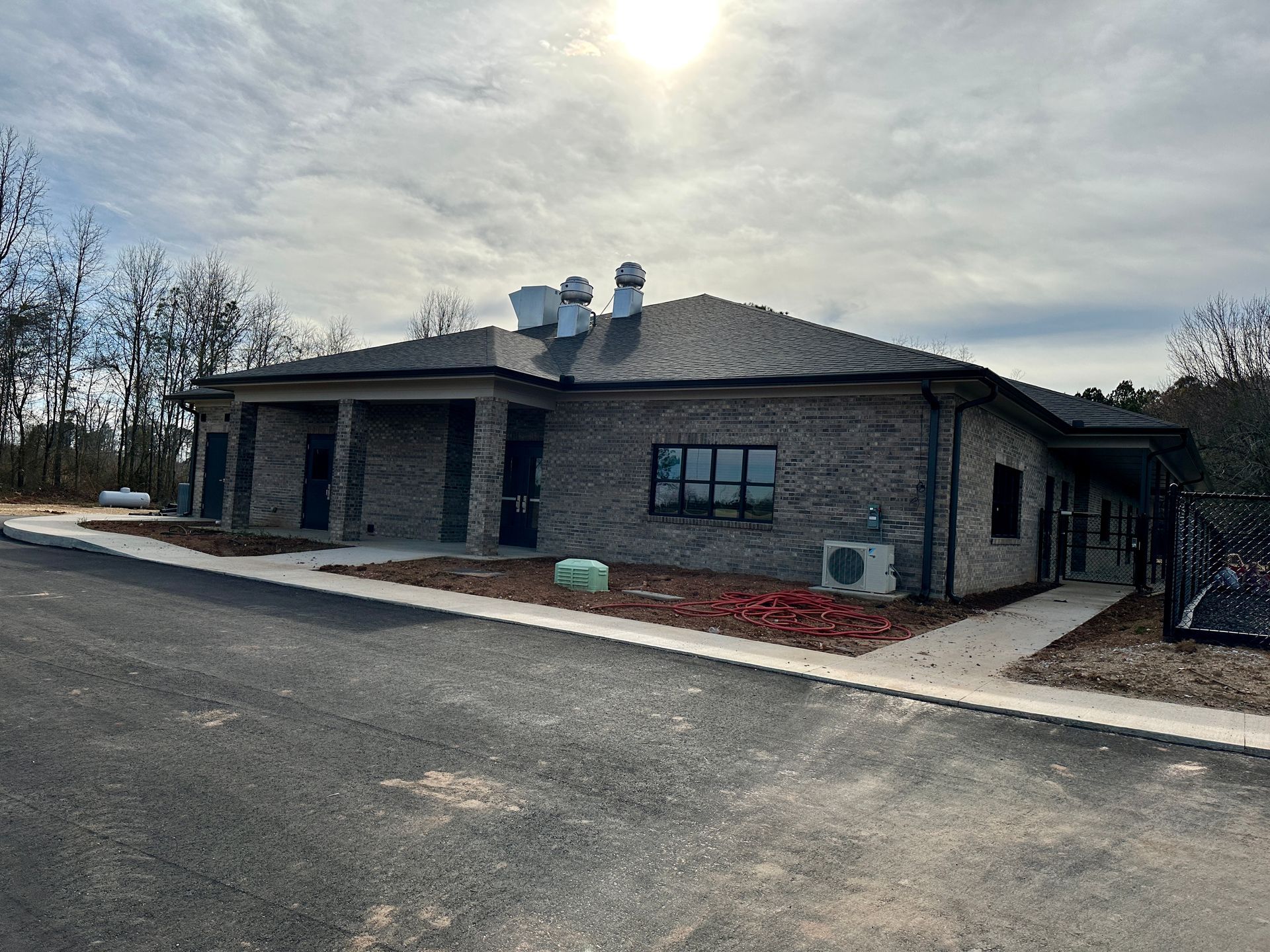 Brick building with a dark roof and a paved driveway under a cloudy sky.