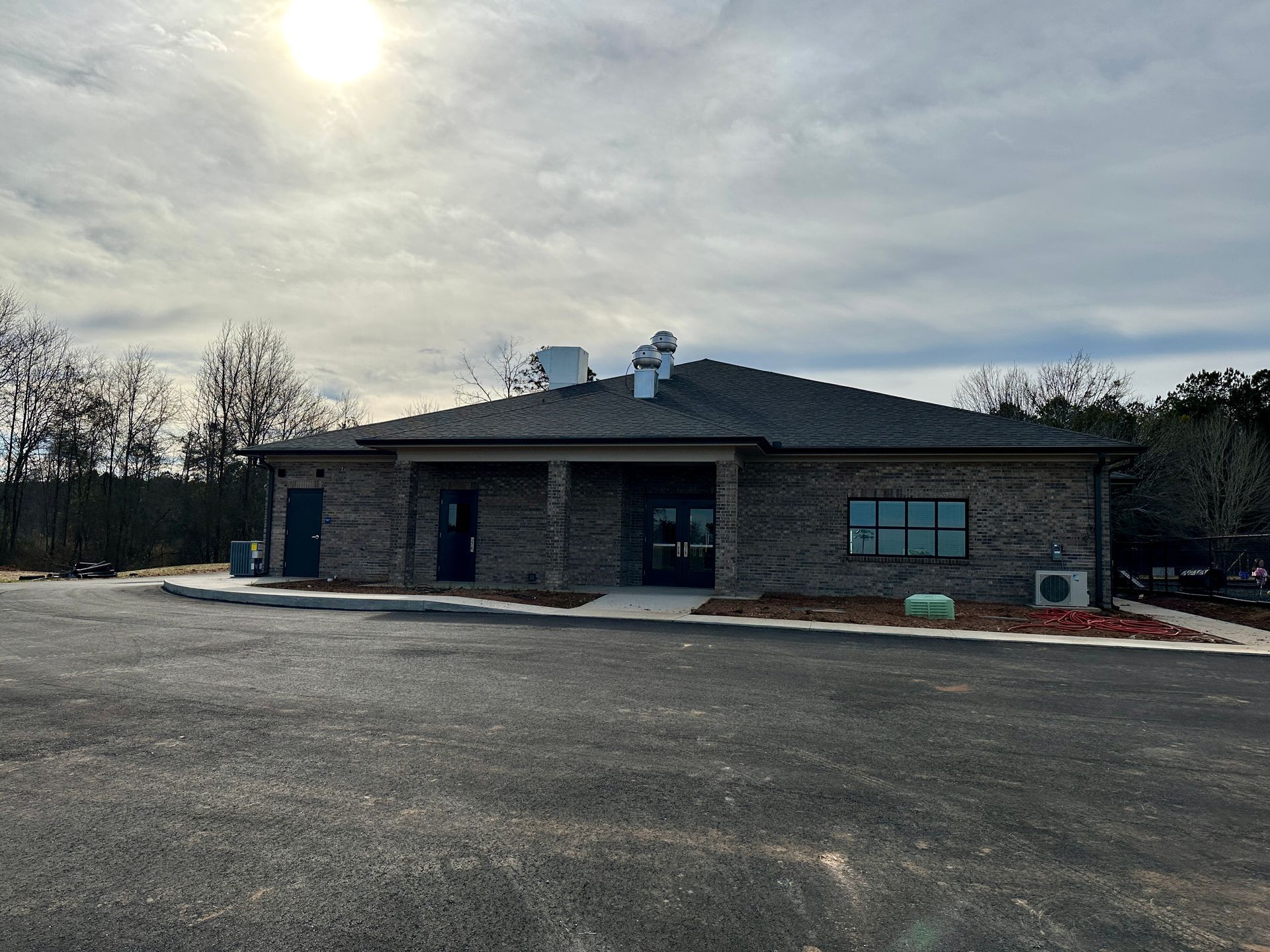 Brick building with a dark roof and small windows, sitting on asphalt with a cloudy sky.