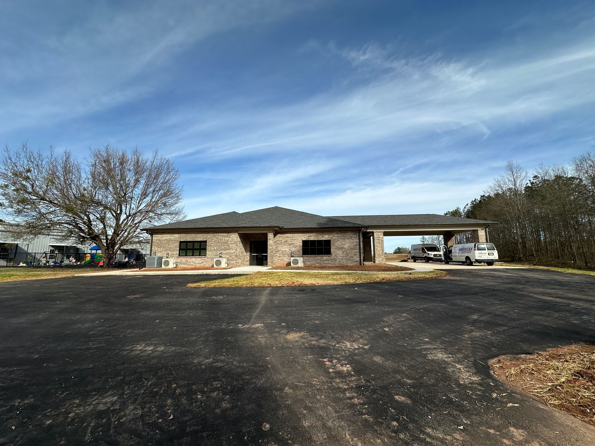 Single-story brick building with a carport. Black asphalt lot under a blue sky.