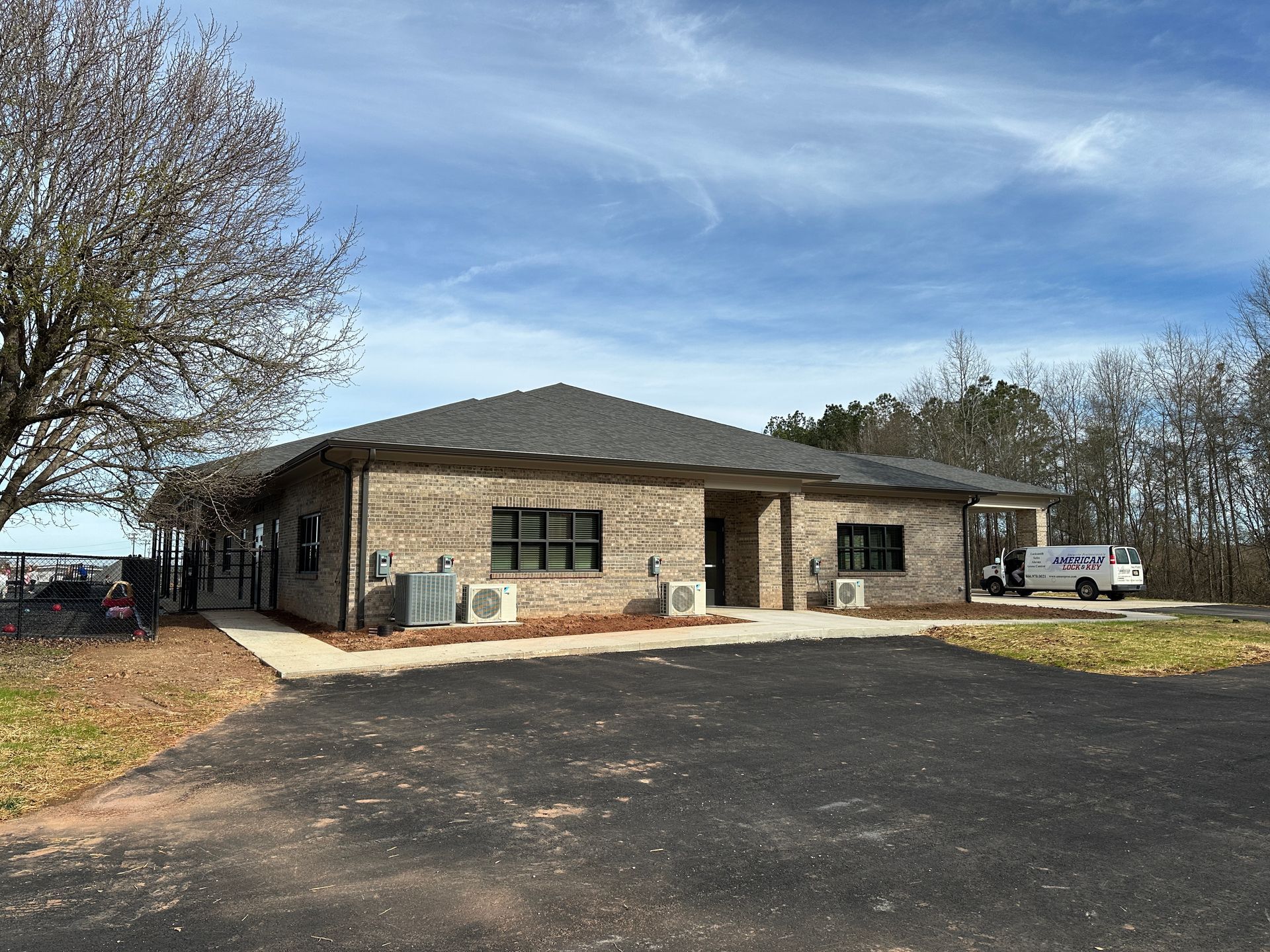 Brick building with black windows and a black asphalt driveway. A service van is parked near the building.
