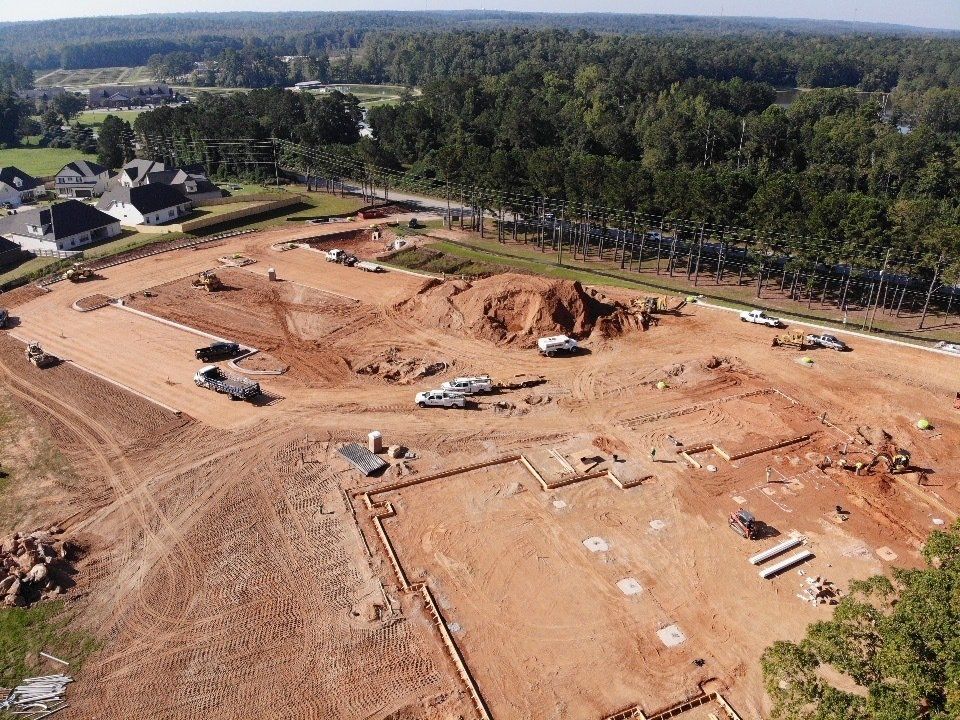 An aerial view of a construction site with a lot of dirt and trees in the background.