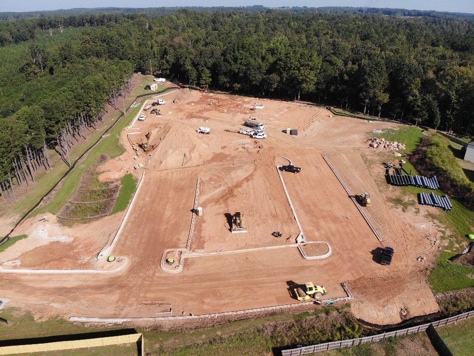 An aerial view of a construction site with a lot of dirt and trees in the background.