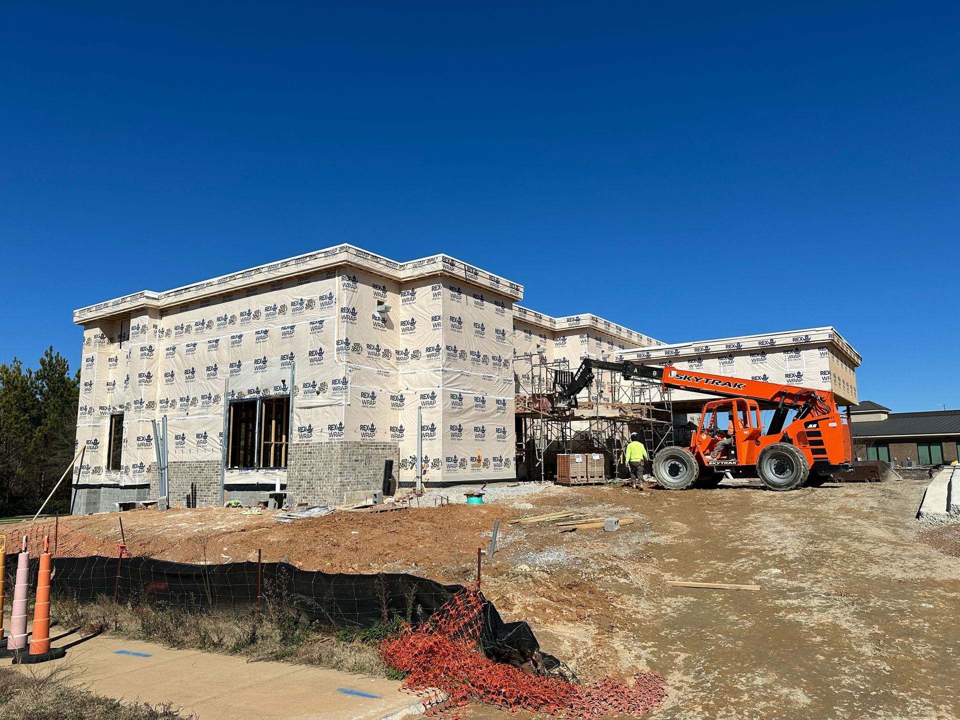 A large house is being built with a forklift in front of it.