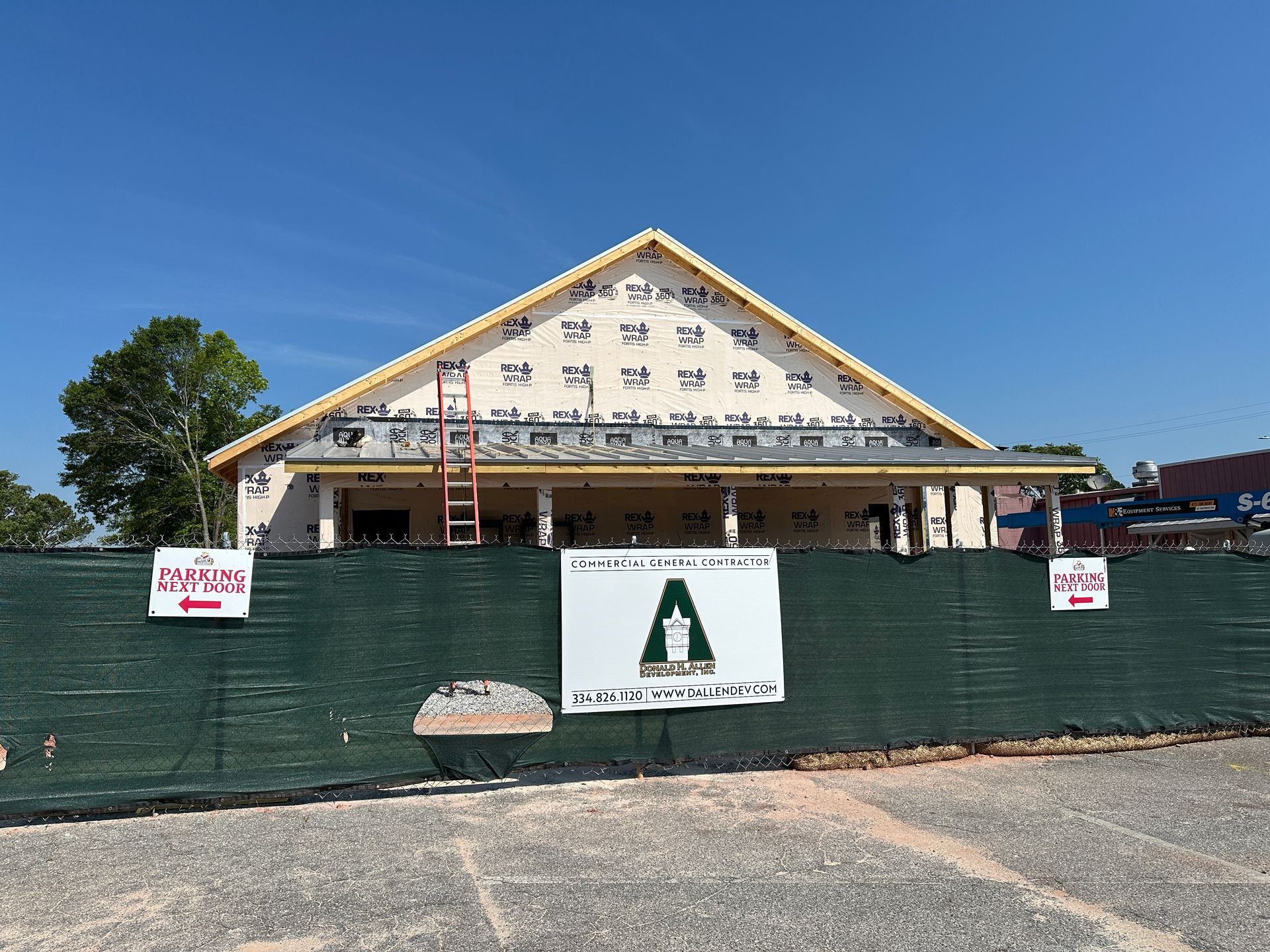A building under construction is behind a green fence.