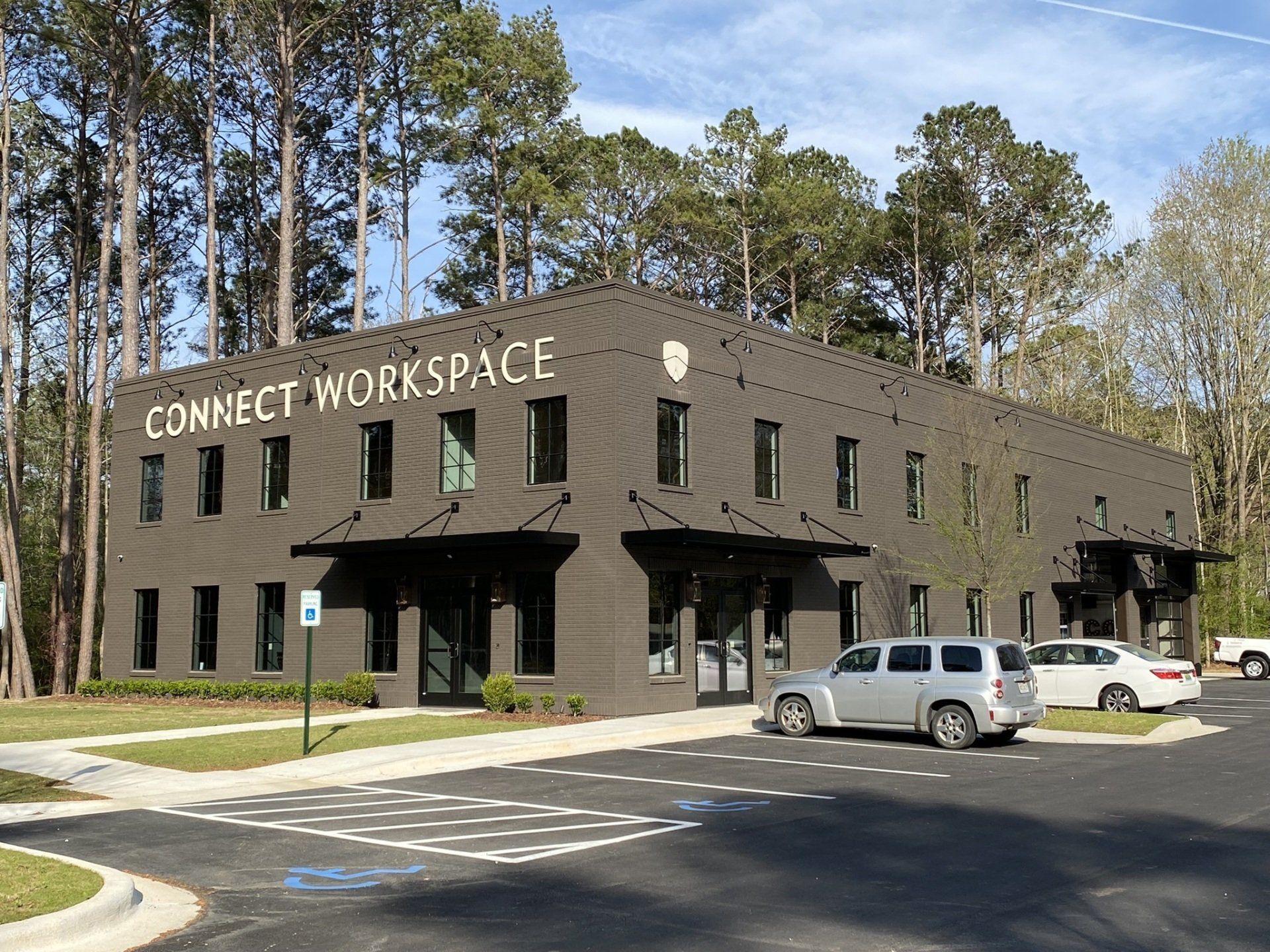 A large brick building with a sign that says connect workspace is surrounded by trees.