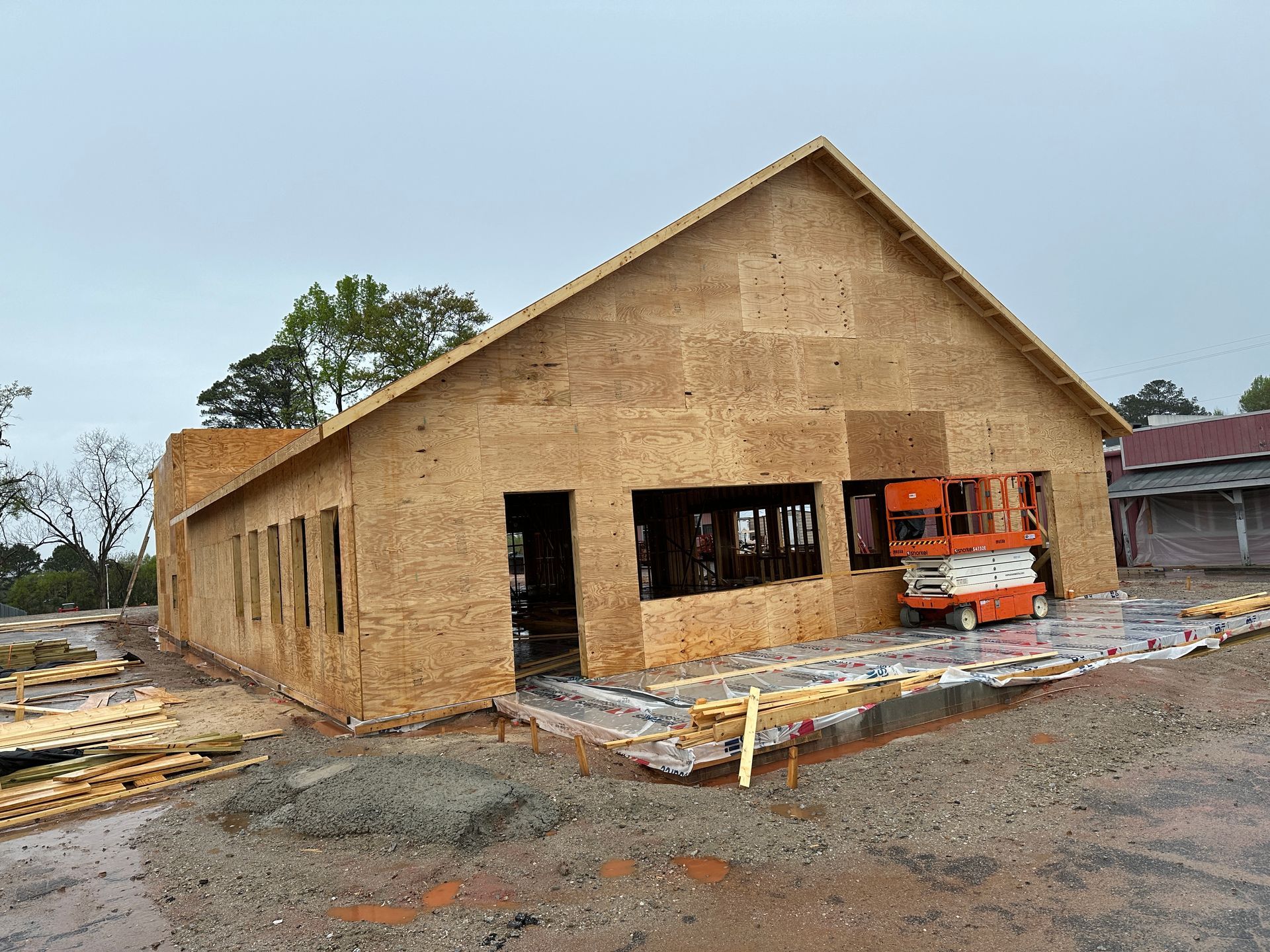 A large wooden house is being built on a dirt lot.