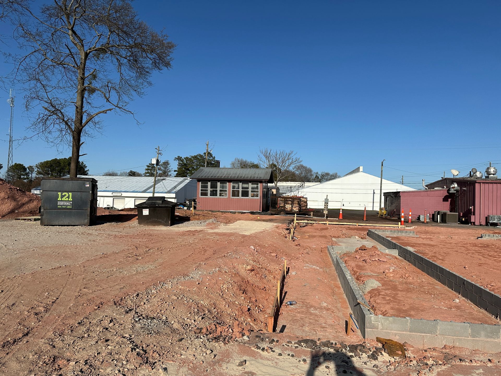 A construction site with a building in the background and a tree in the foreground.