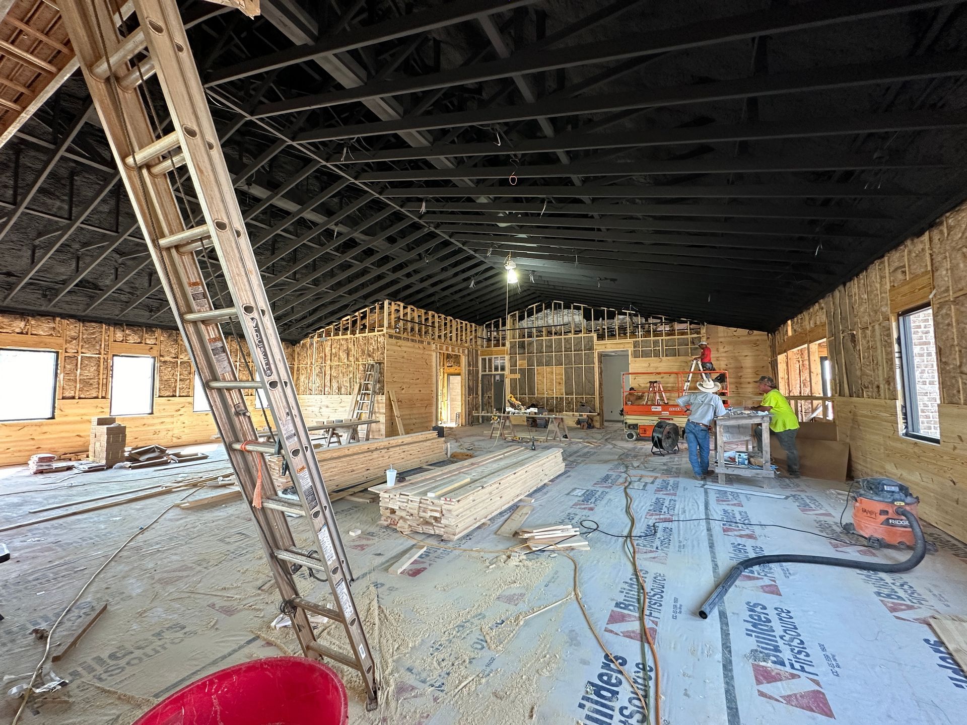 A large room under construction with a ladder and a red bucket.