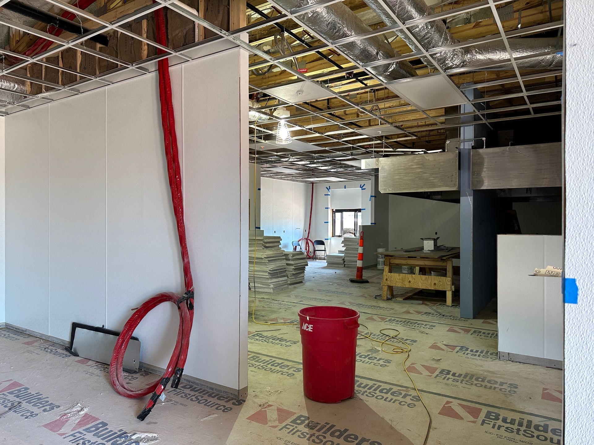 A red trash can is sitting on the floor of a building under construction.