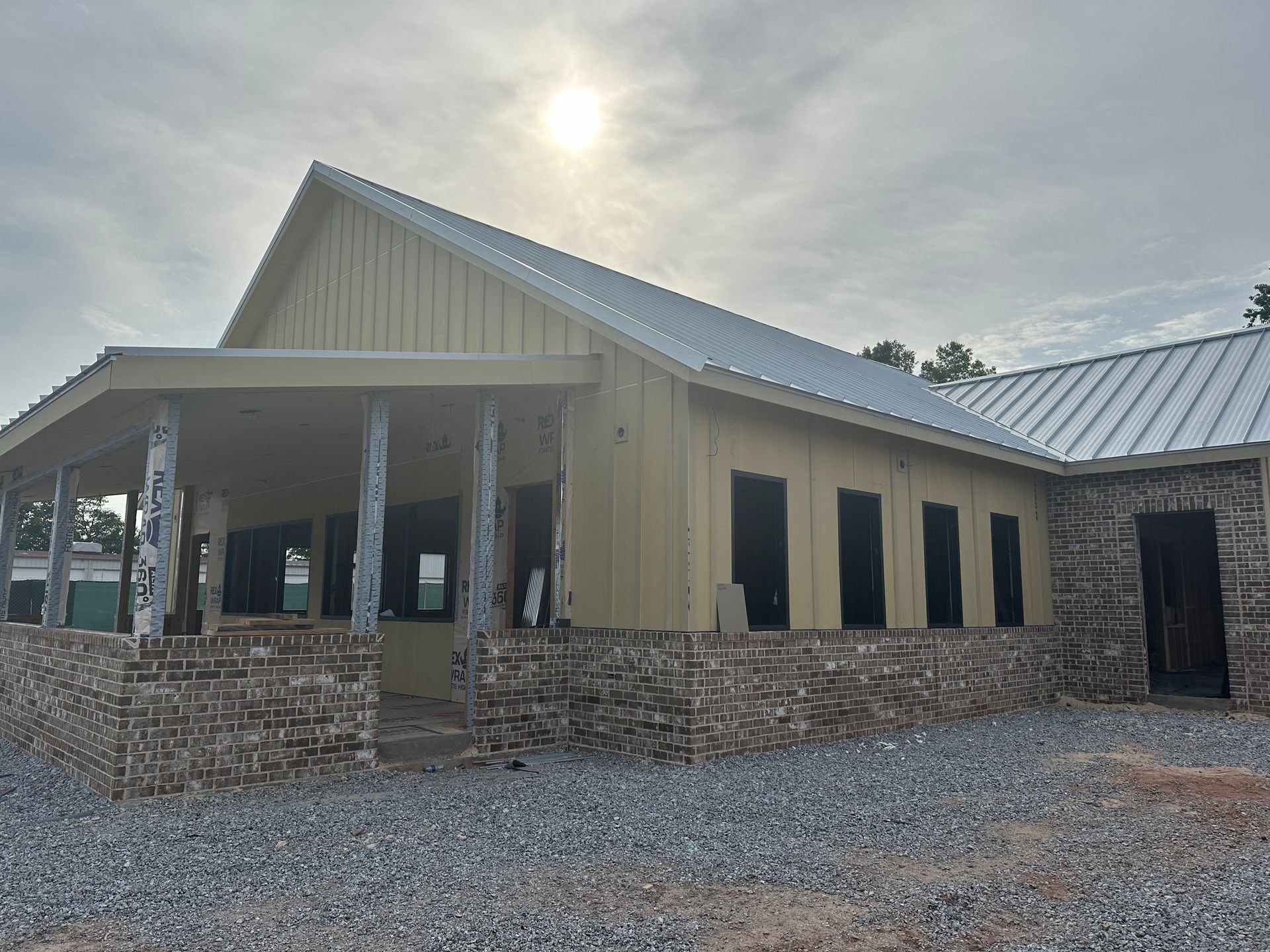 A large house with a metal roof and a stone wall is being built.