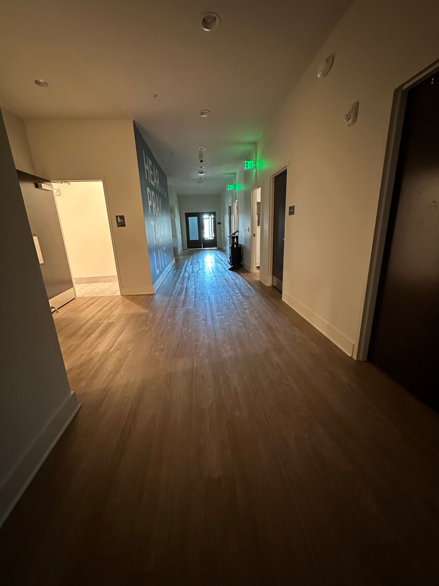 A long hallway with wooden floors and a green exit sign.