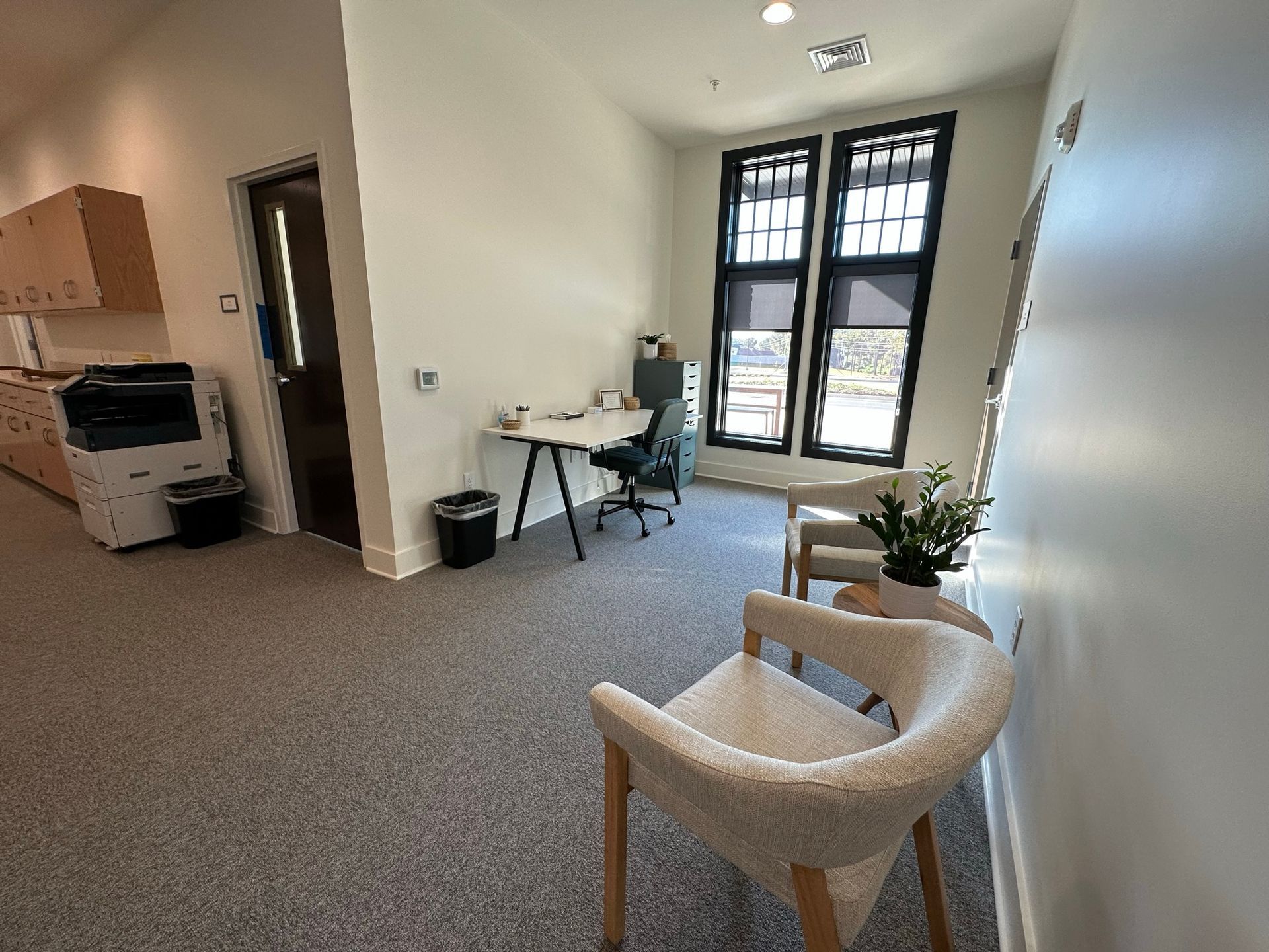 A room with a desk , chairs , and a printer.