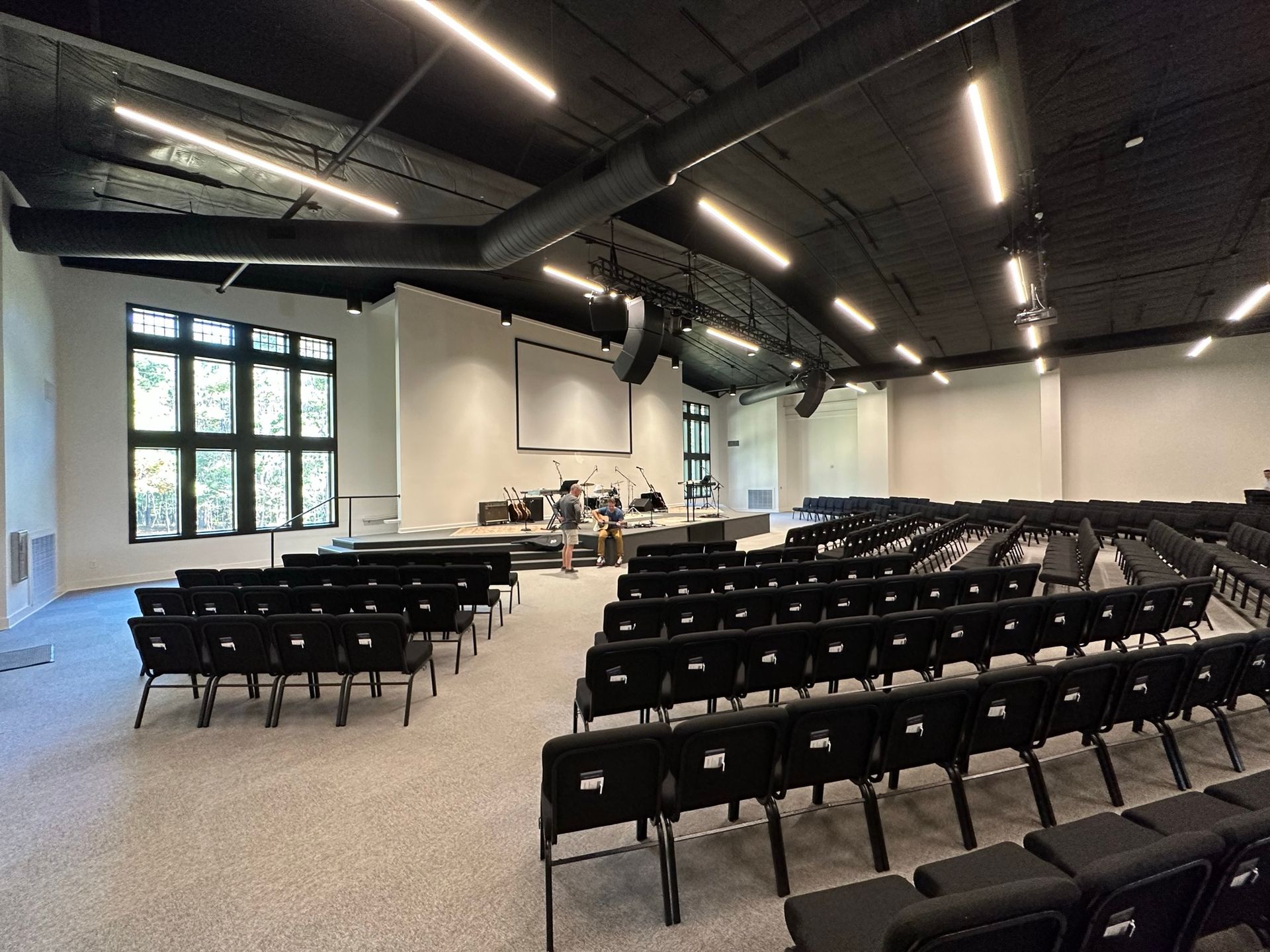 A large auditorium with rows of black chairs and a projector screen.