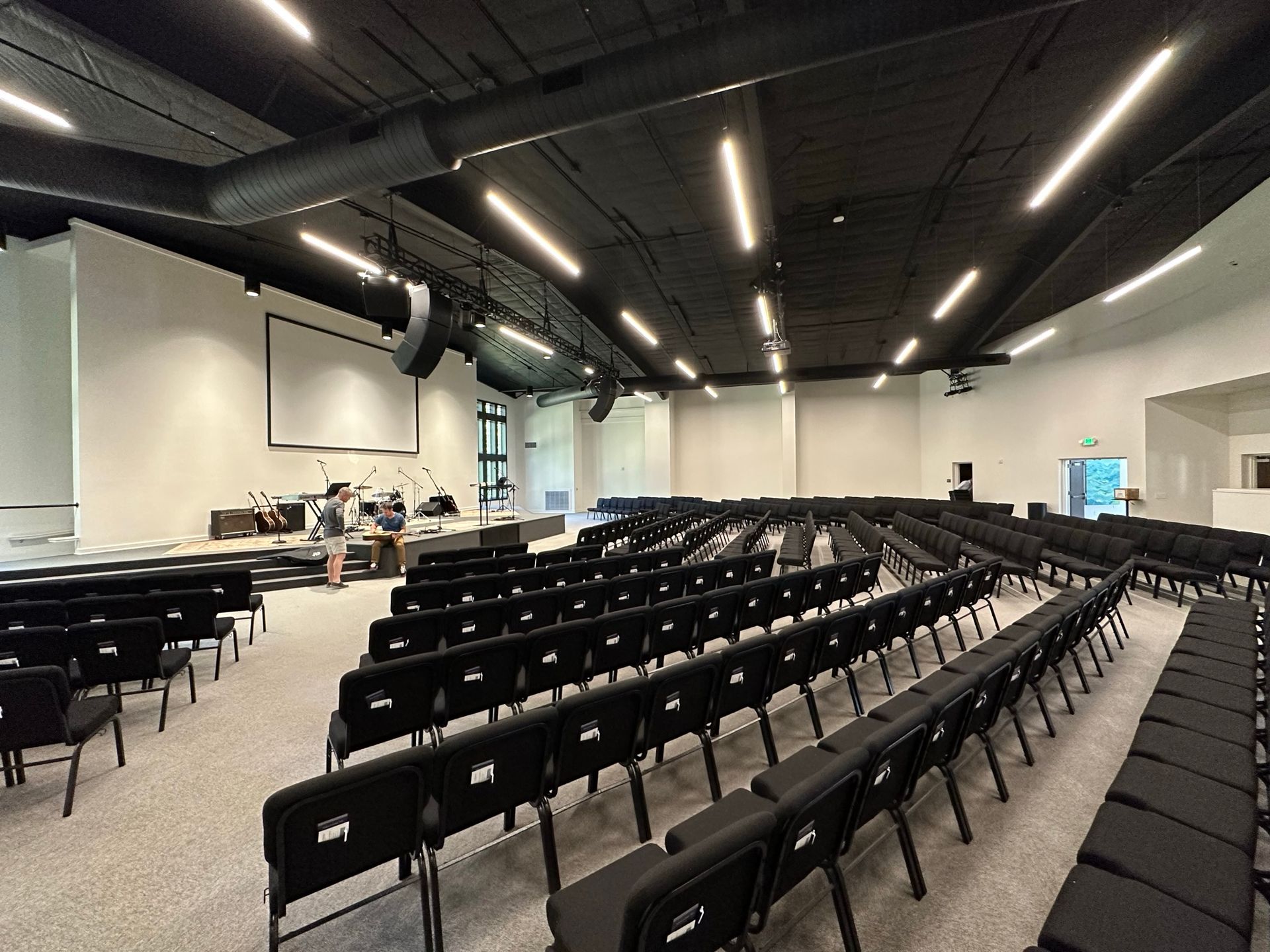 A large auditorium with rows of black chairs and a projector screen.