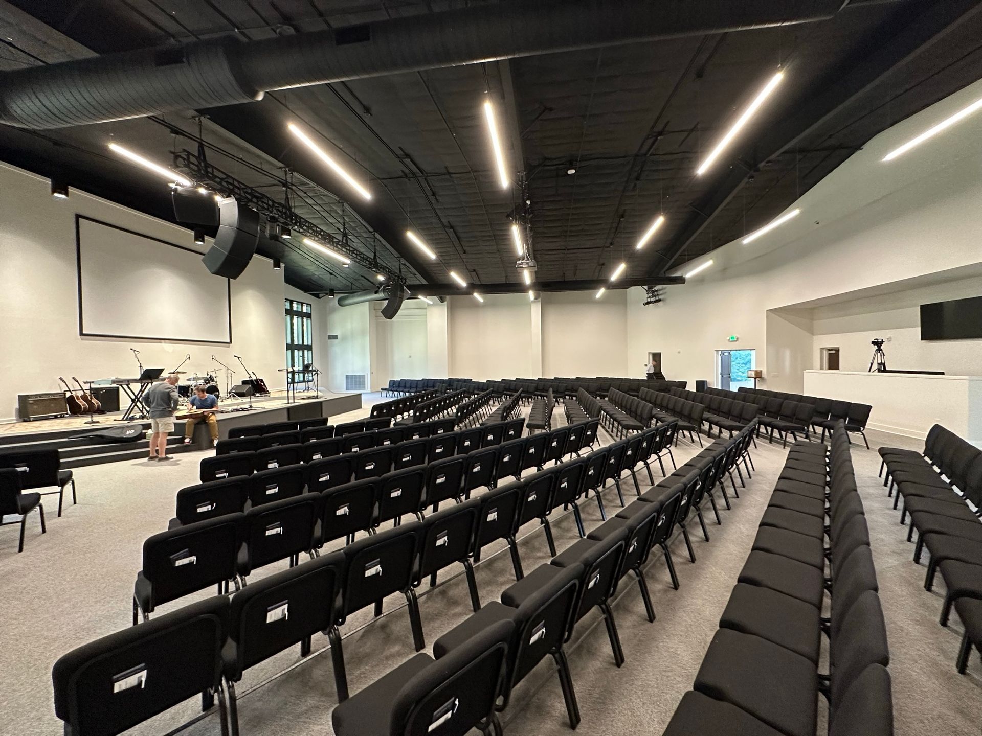 A large auditorium with rows of black chairs and a projector screen.