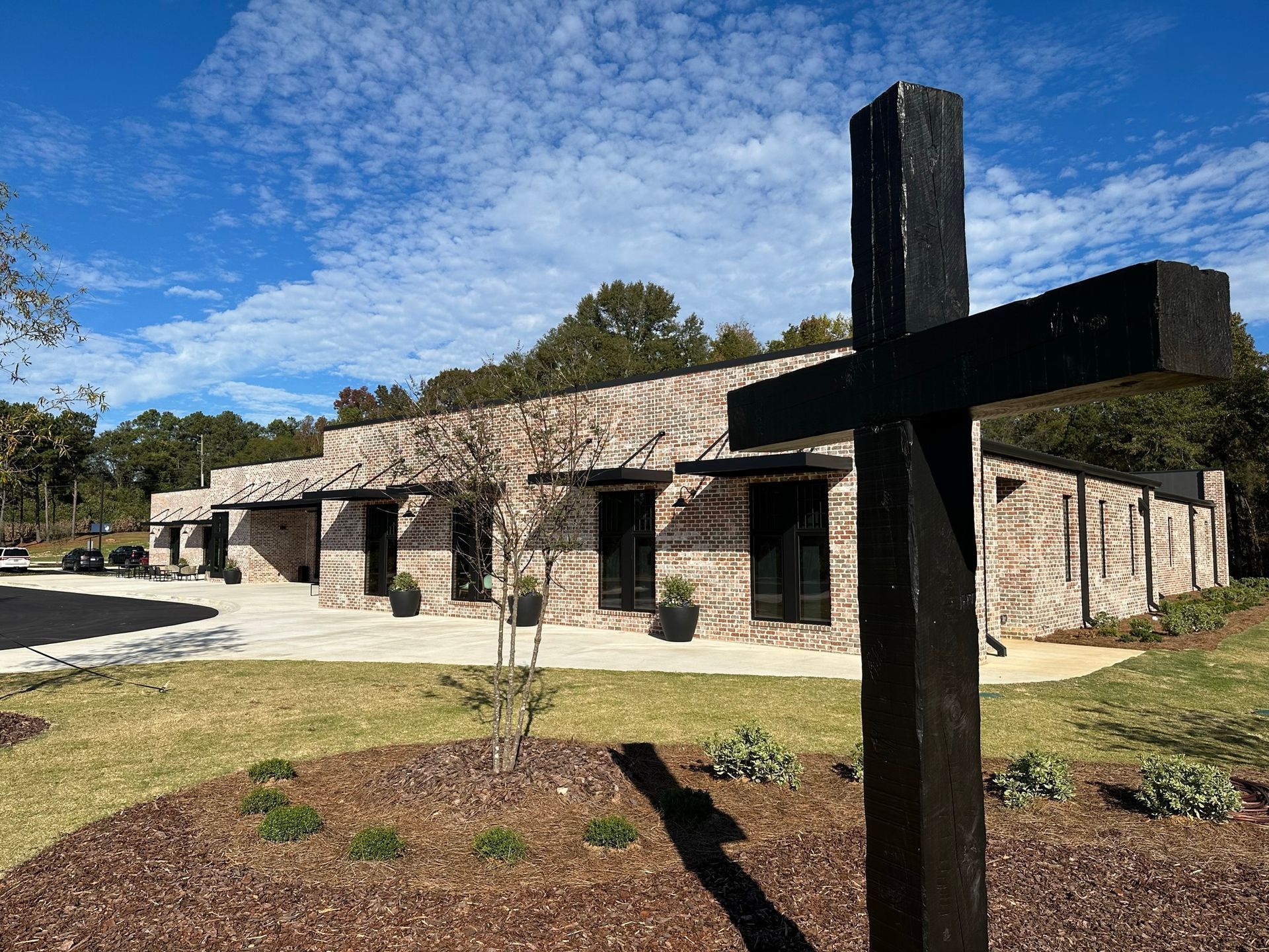 A black wooden cross is in front of a brick building.