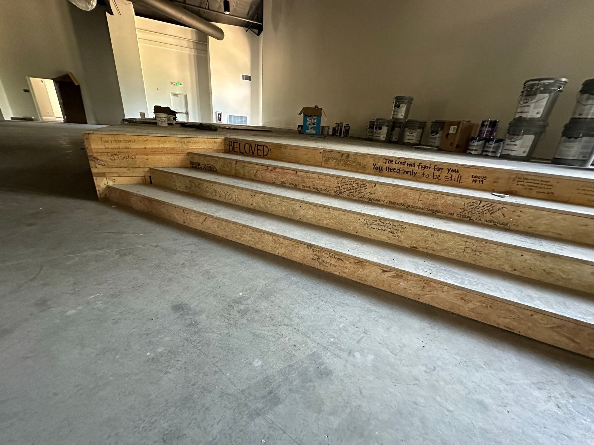 A set of wooden stairs in a room with paint cans on the floor.
