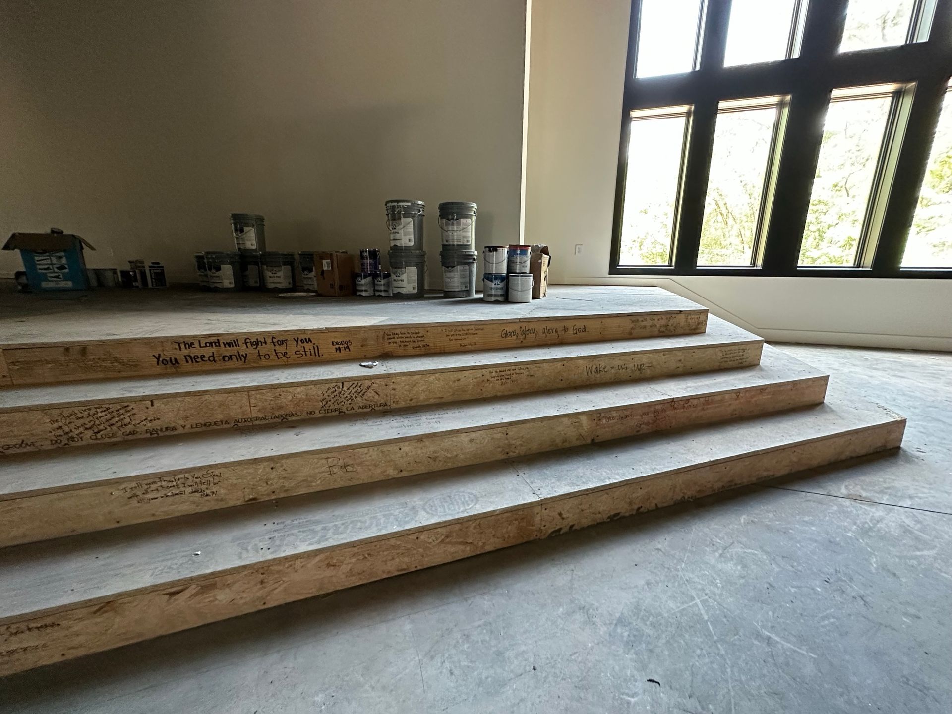 A room with wooden stairs and paint cans on the floor