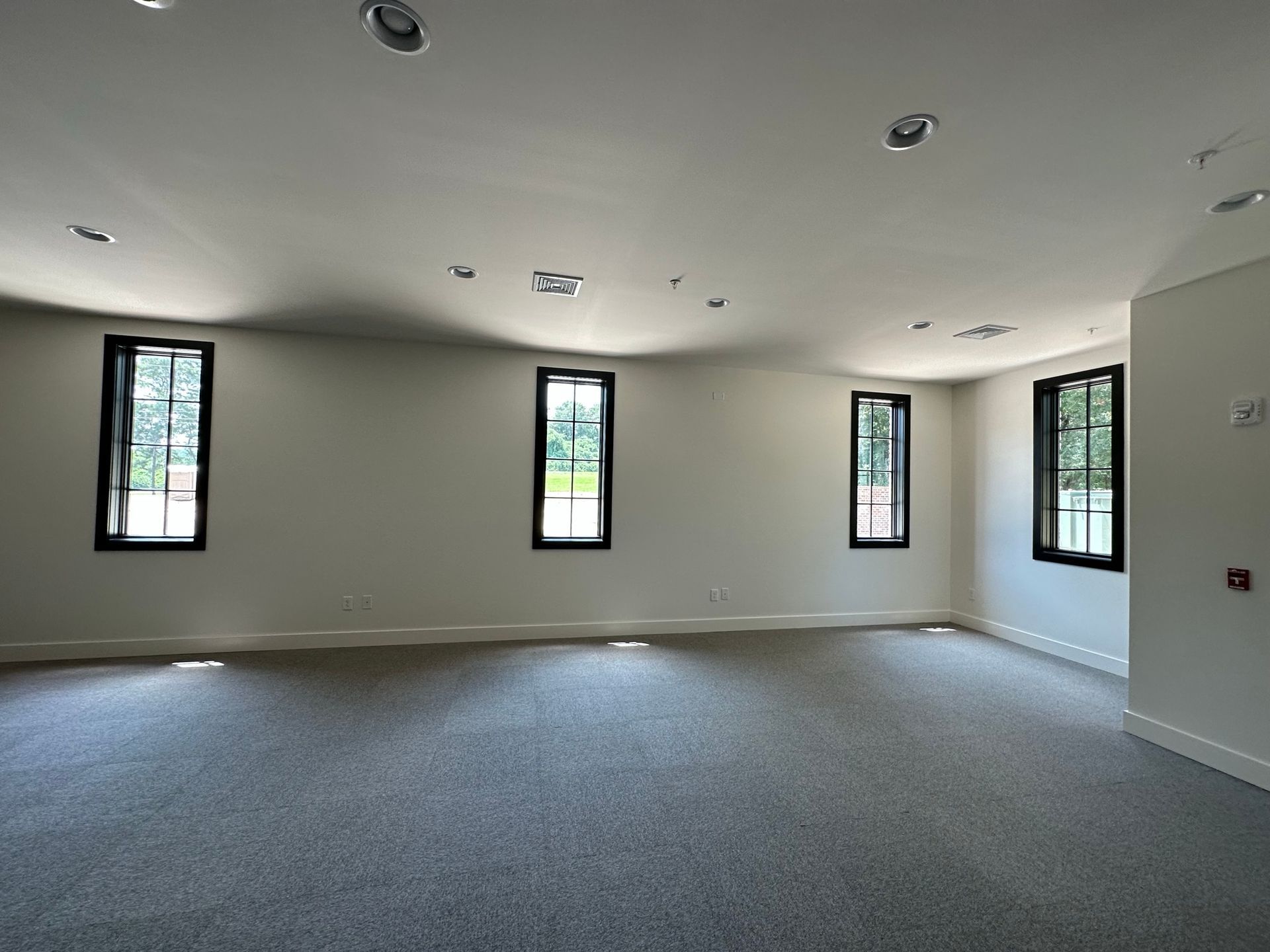 An empty room with a lot of windows and a carpeted floor.